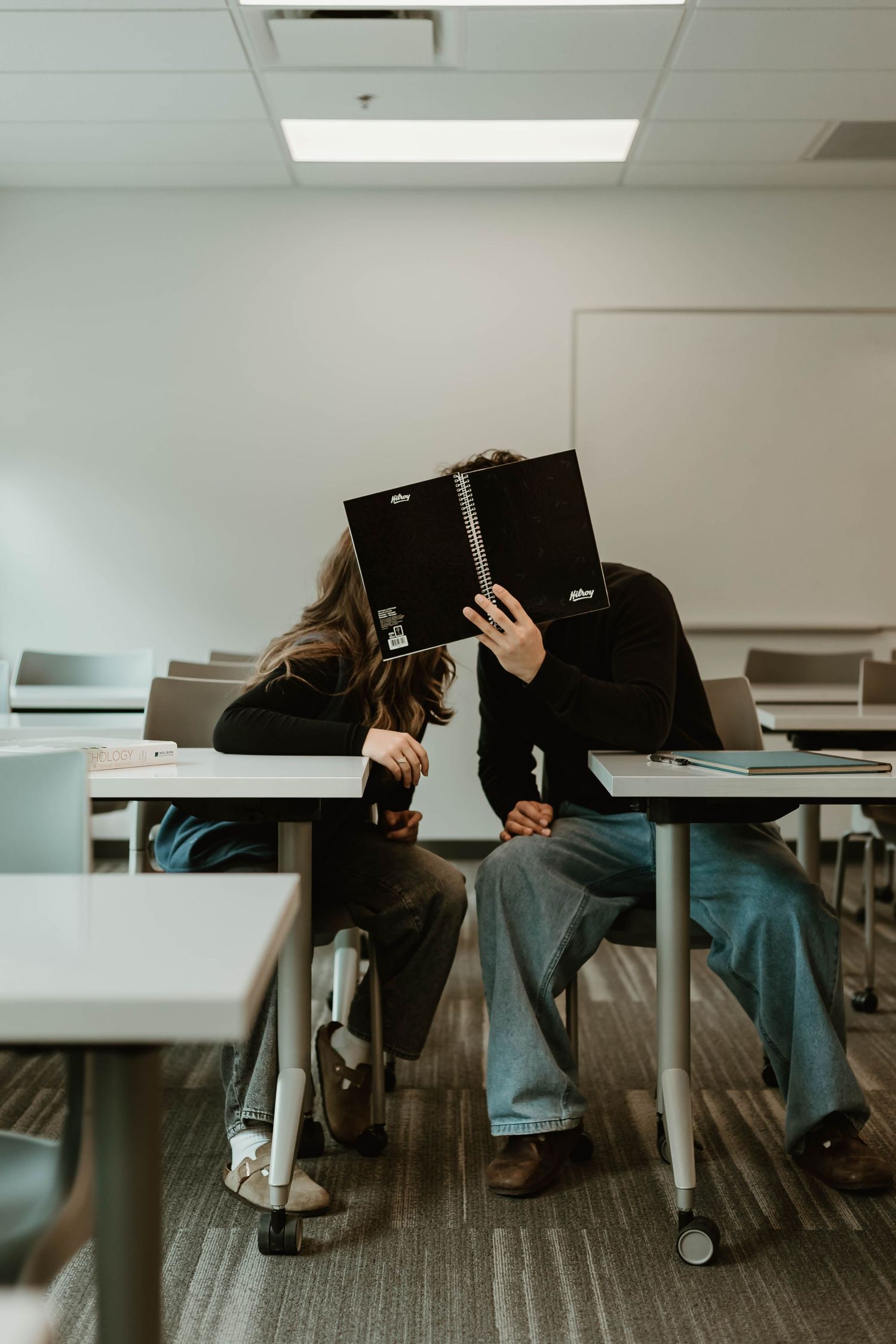 Students sit at desks in a classroom with their heads resting on textbooks during a study break.