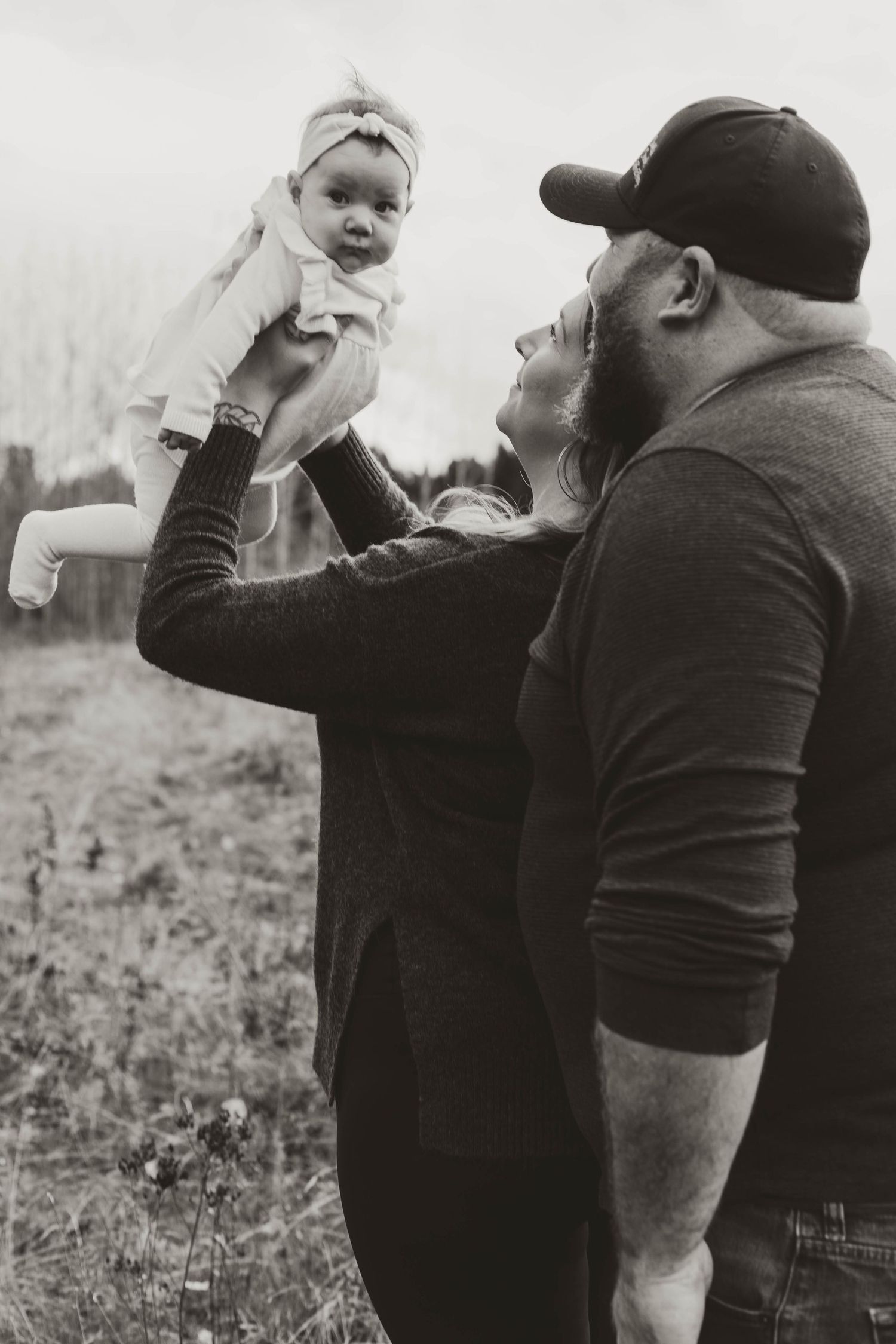 Black and white photo of a baby being lifted playfully outdoors by an adult.