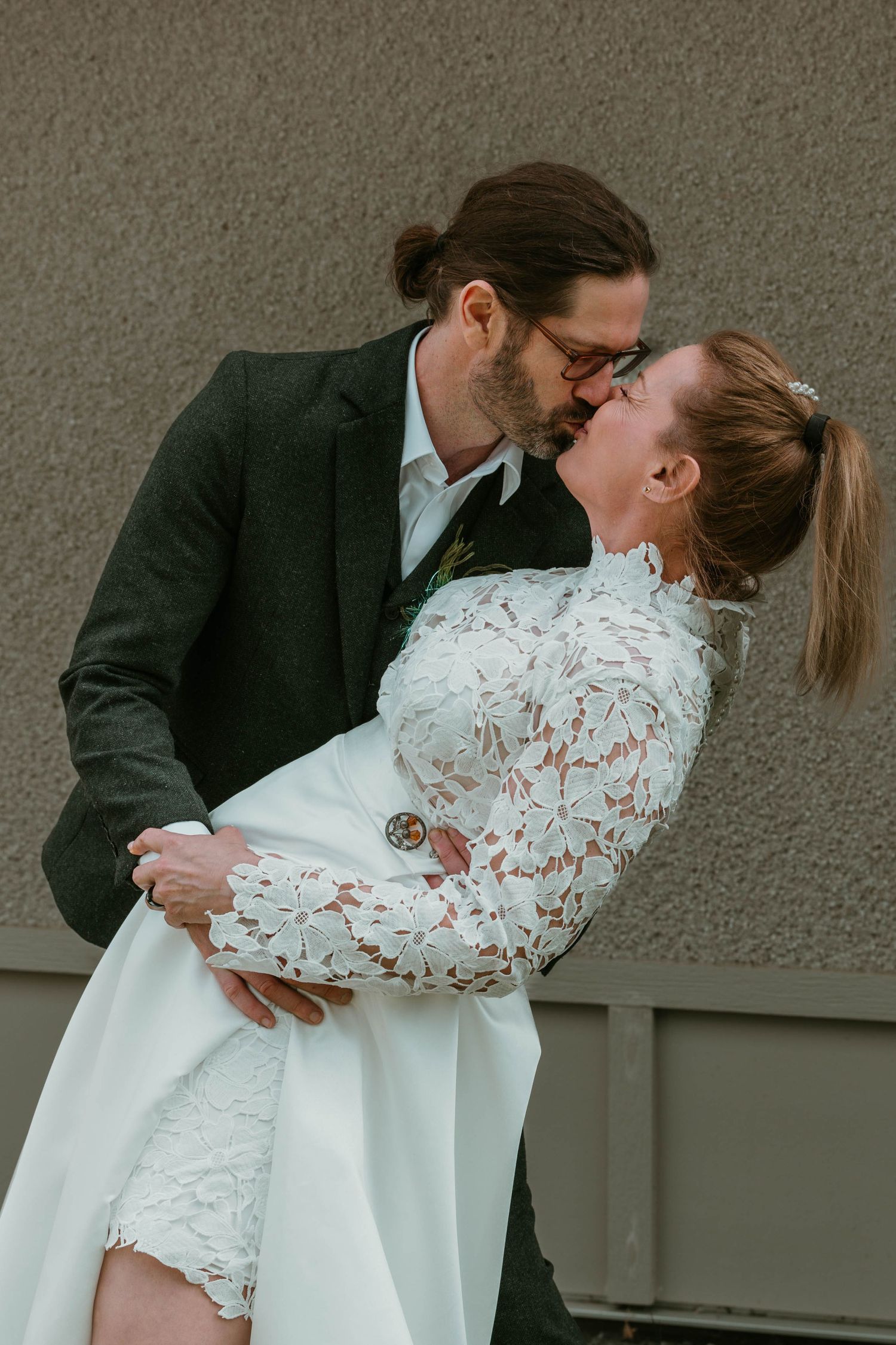 Romantic dip kiss between newlyweds, bride wearing lace long sleeve dress.