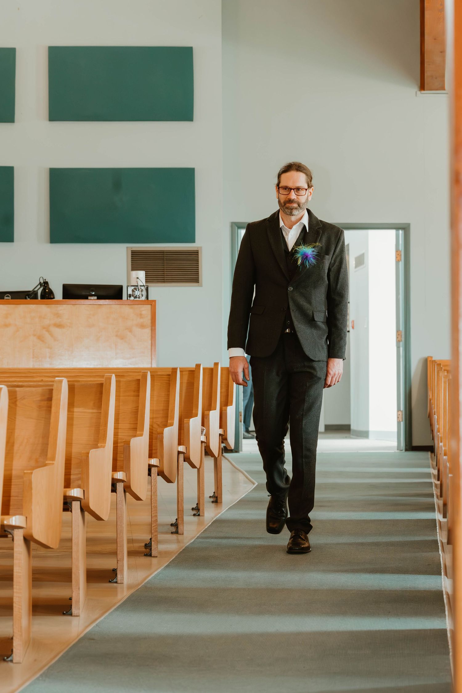 A person in a dark suit walks down a church aisle with green panels on the wall.