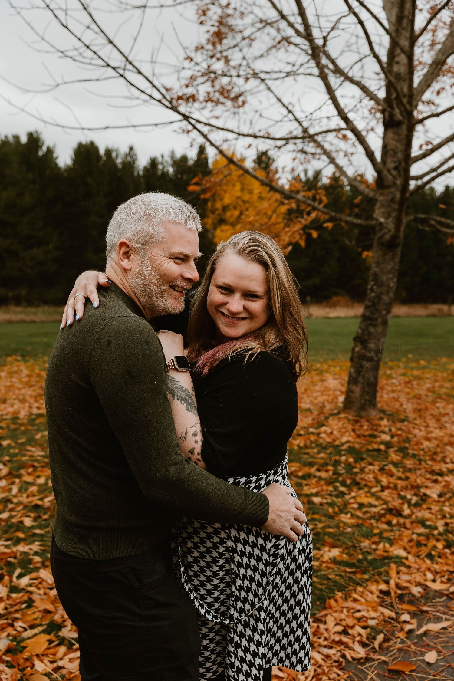 A couple embraces among fallen autumn leaves while sharing a tender moment in a park.