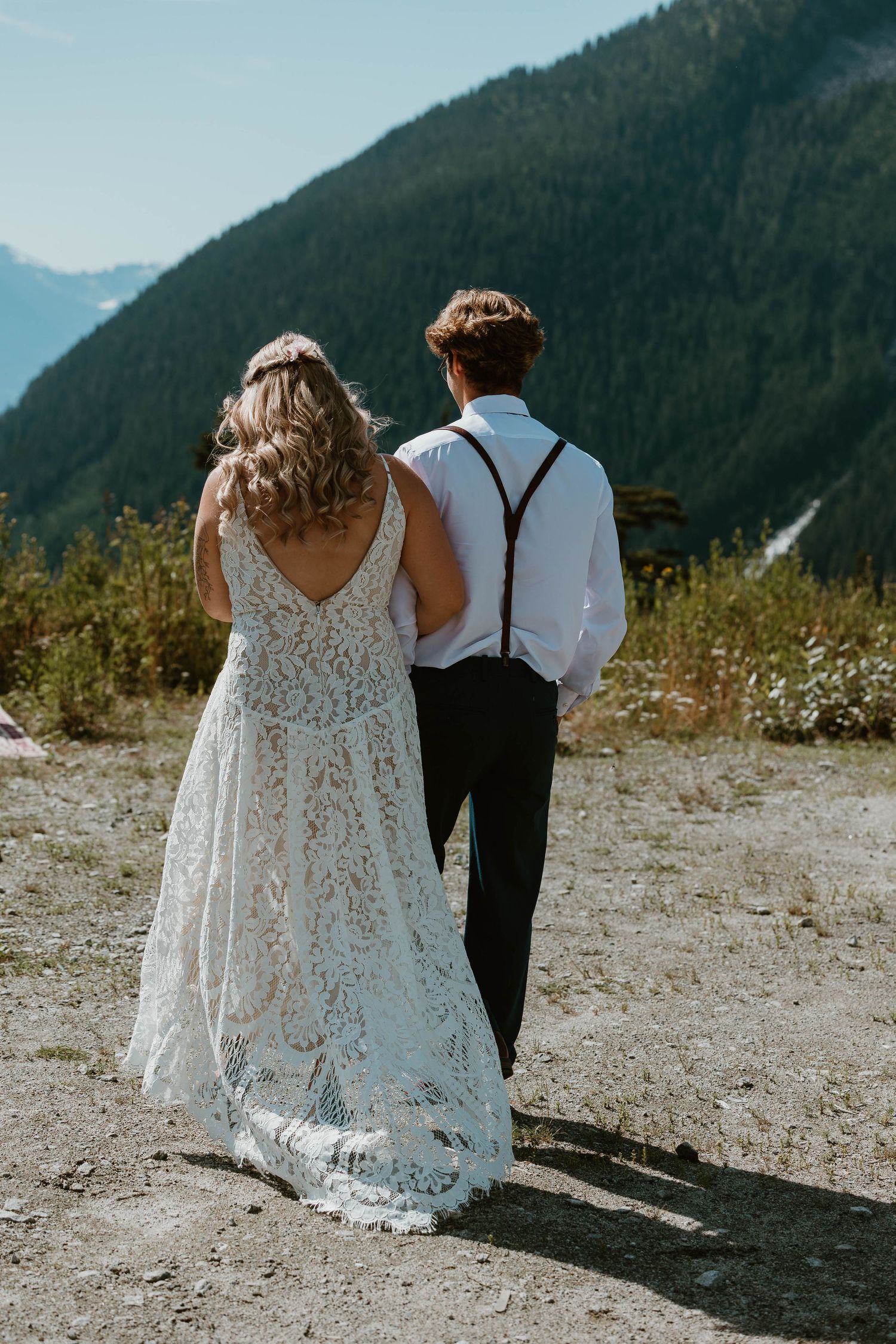 Couple in wedding attire standing on mountain overlook with scenic vista.