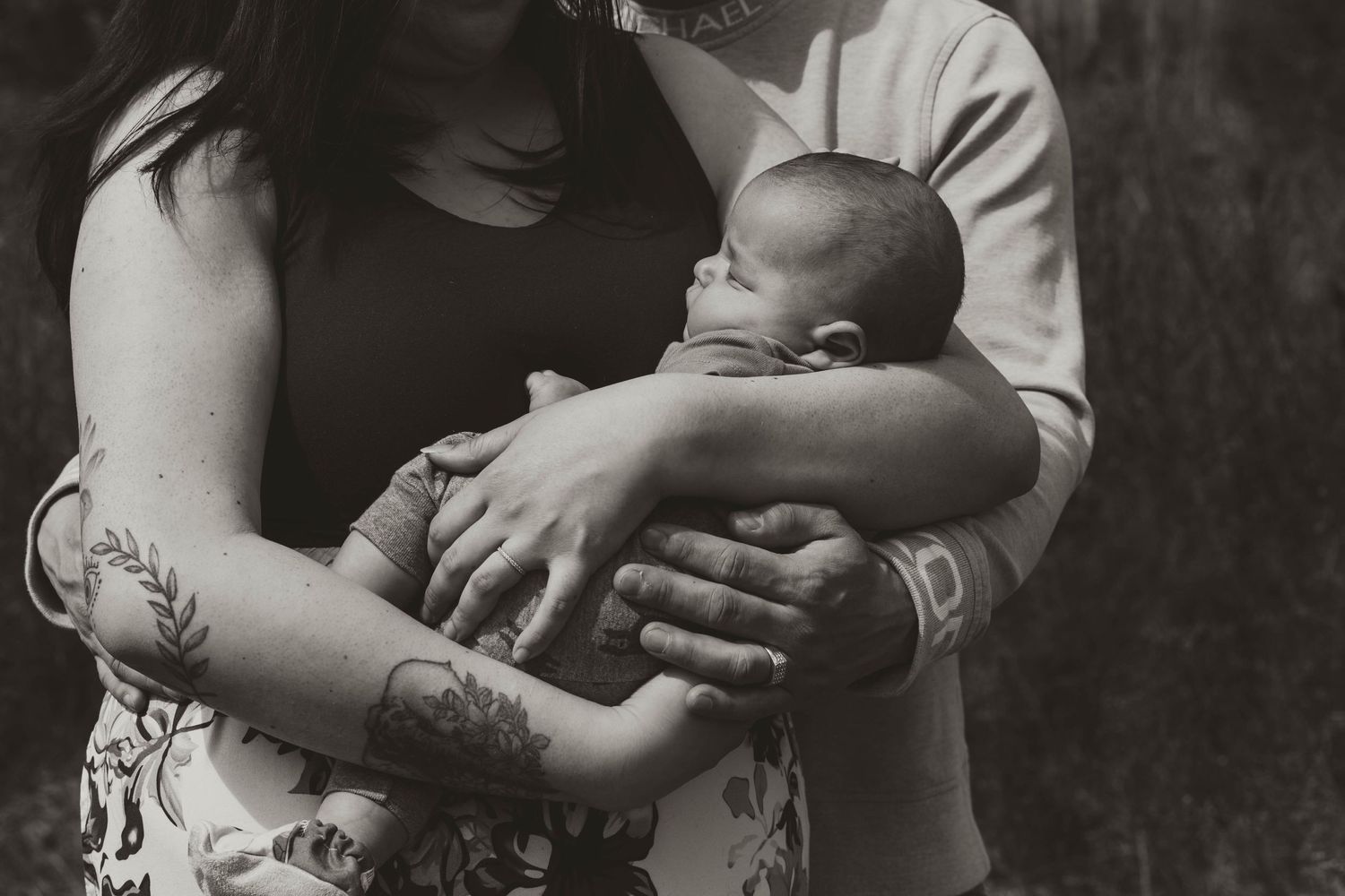 An intimate black and white portrait of a newborn being cradled by tattooed arms.