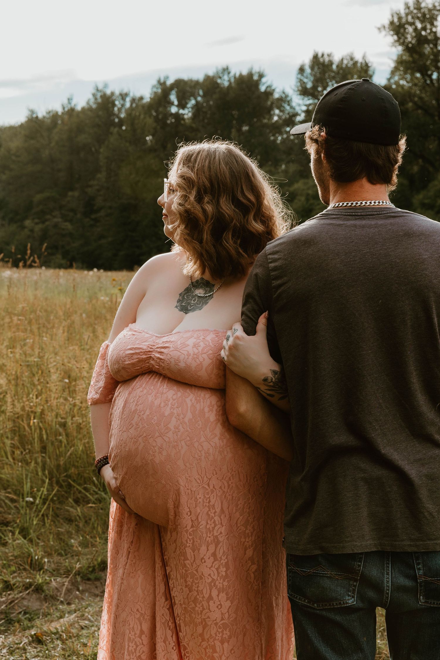 A couple shares an intimate moment in a sunlit field, with the person wearing a flowing peach-colored dress.