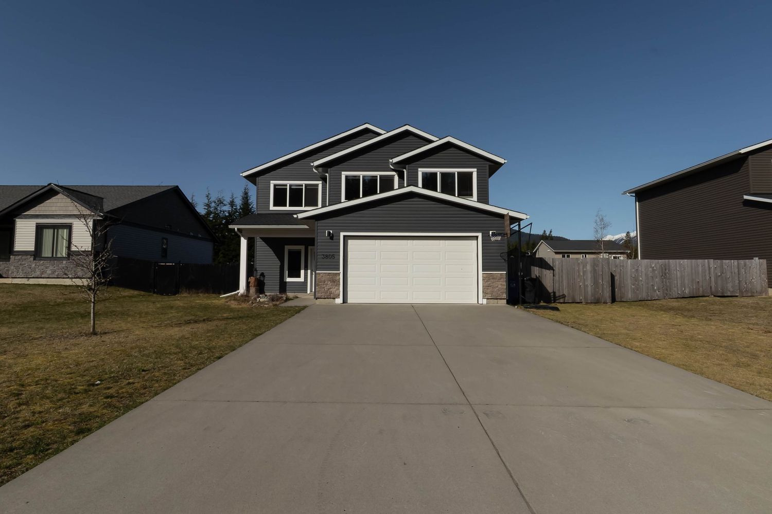 Modern two-story house with gray siding, white trim, and attached double garage on concrete driveway on sunny day.