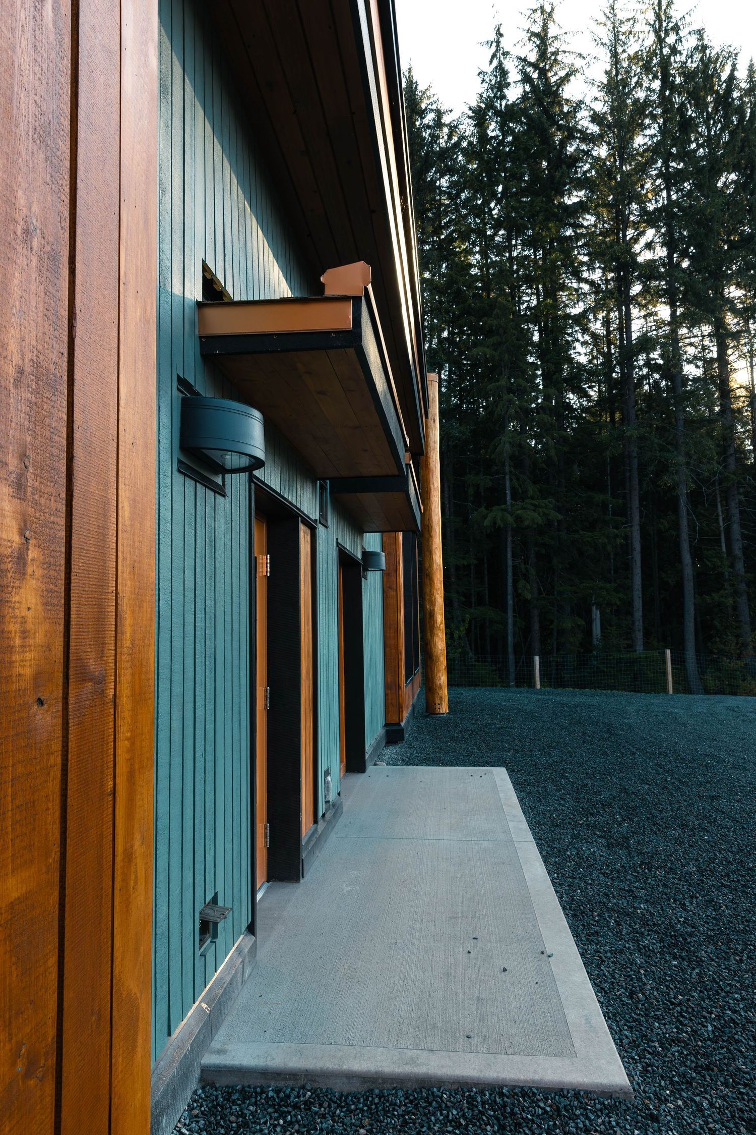 Wooden building exterior with teal accents and concrete walkway against a forest backdrop.