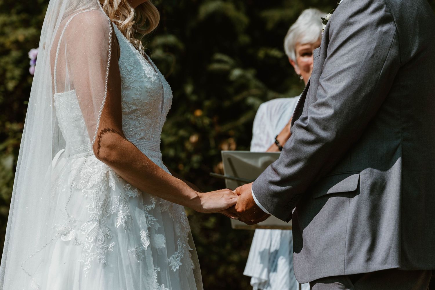 Intimate moment of couple holding hands during outdoor wedding ceremony.