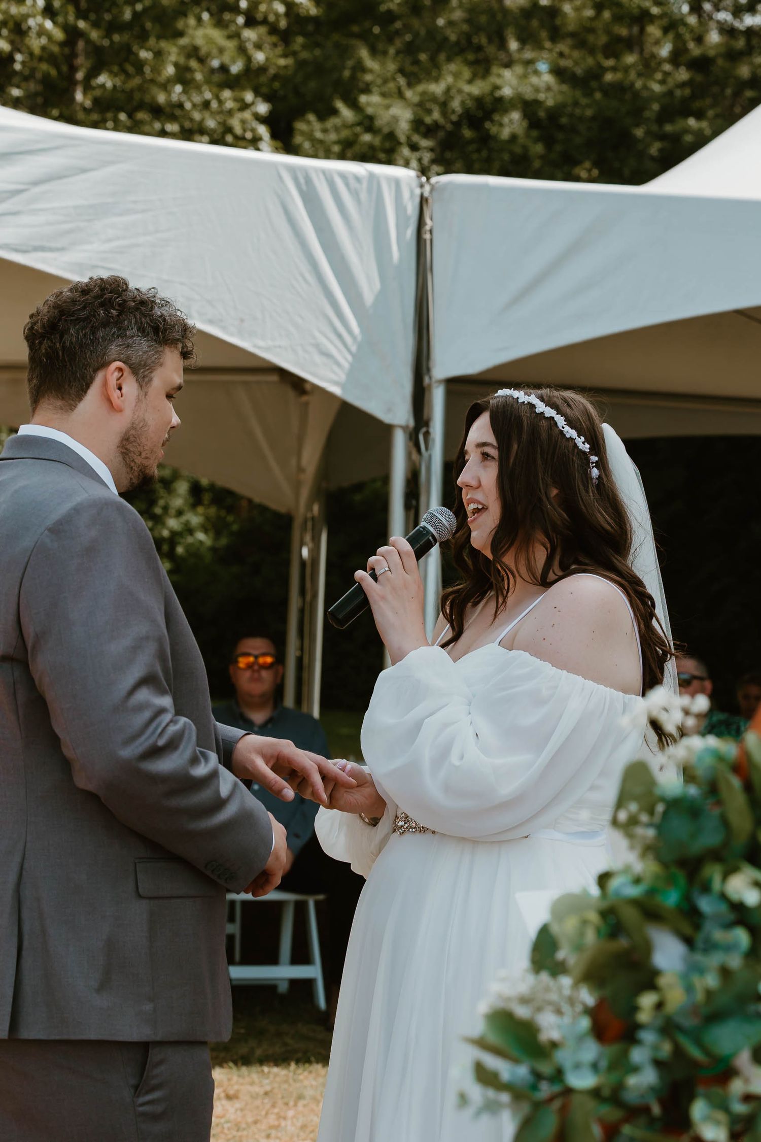 Couple exchanging vows under white tent during outdoor wedding ceremony.