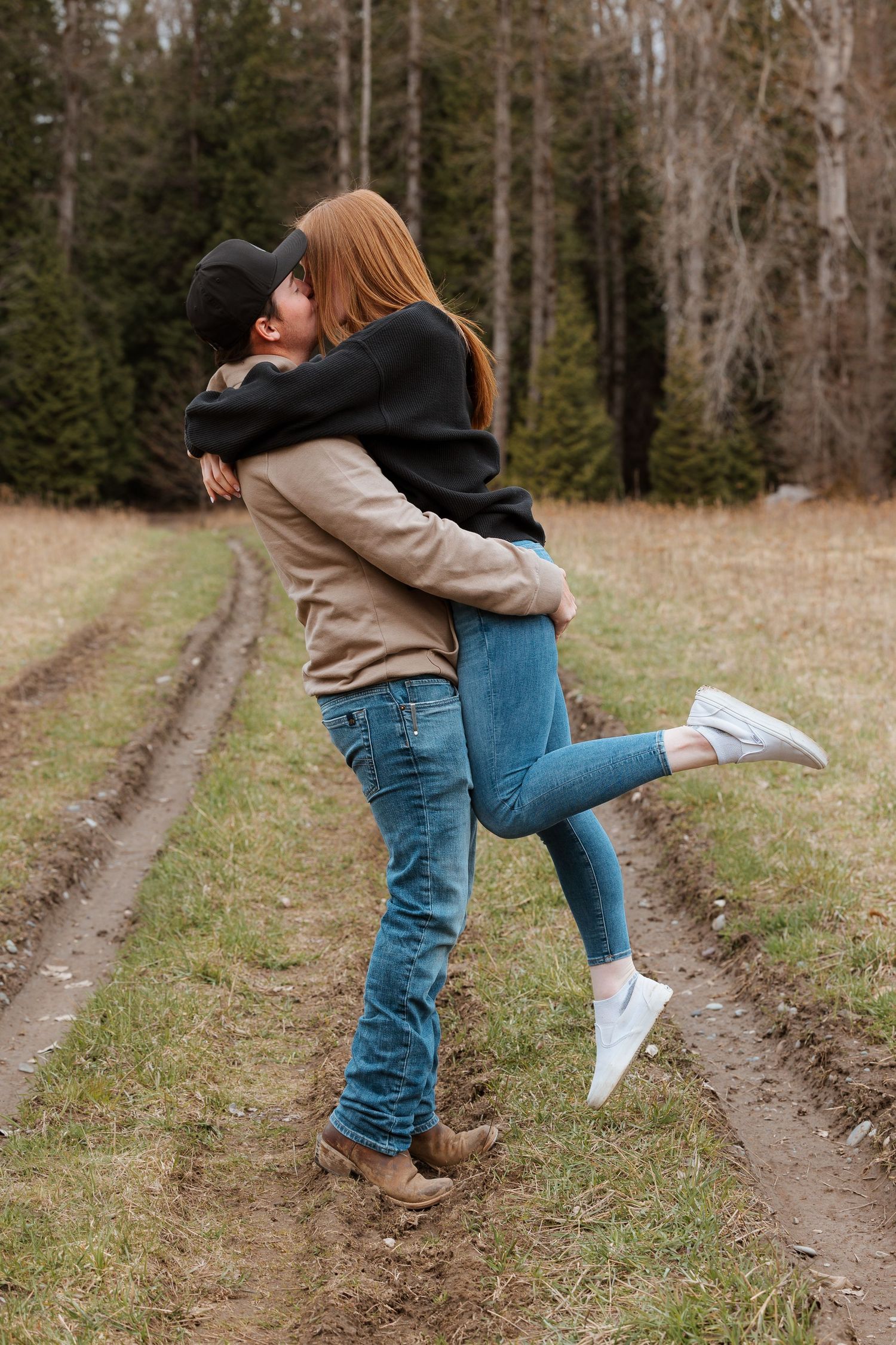Romantic couple embrace and spin in dirt path with forest backdrop.