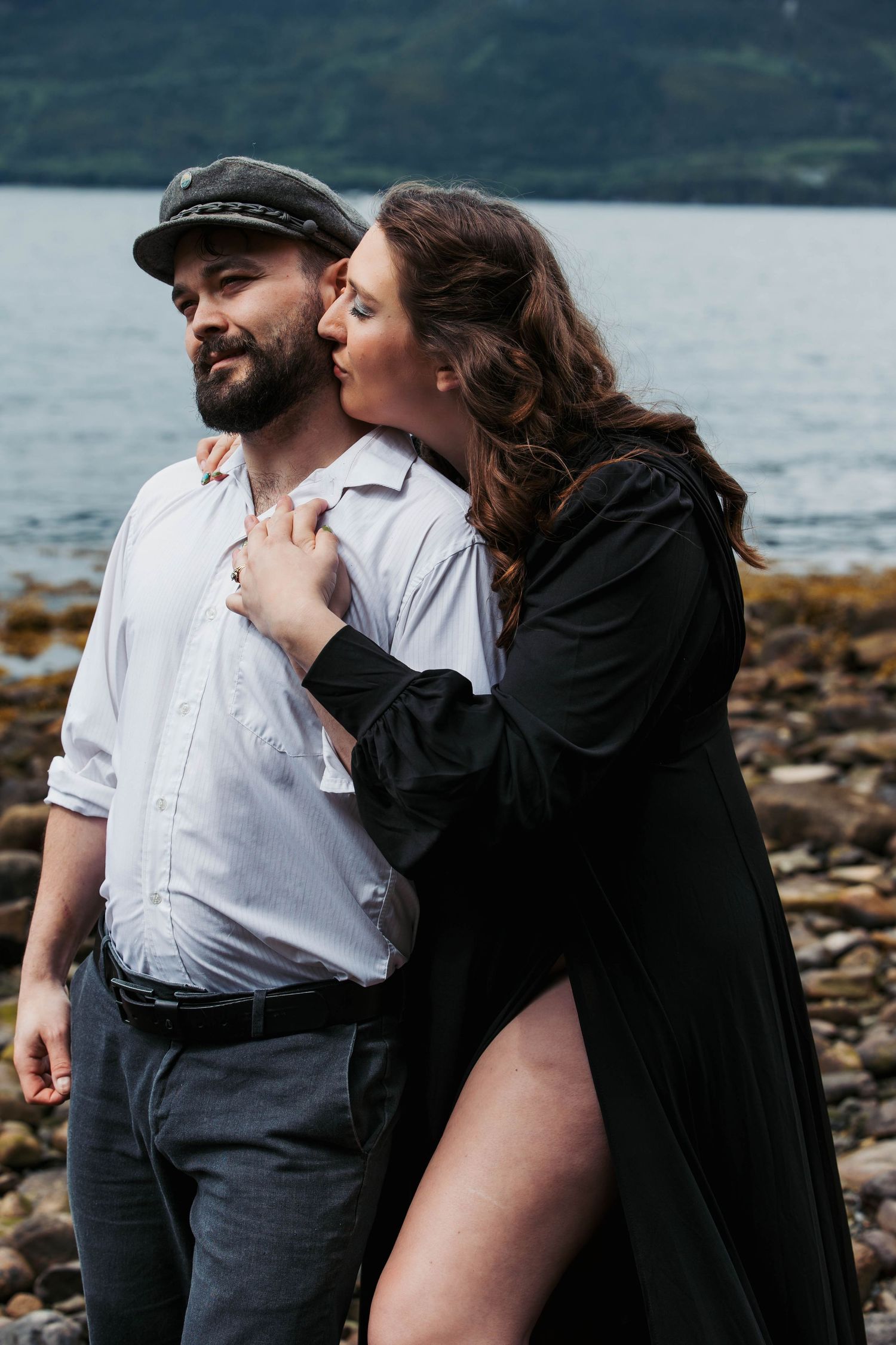 An intimate moment shared between couple on rocky beach with ocean backdrop.
