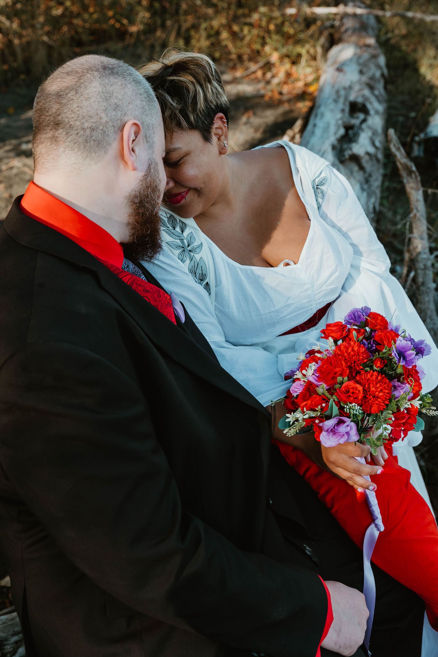 Intimate moment between newlyweds with vibrant red and purple bouquet outdoors.