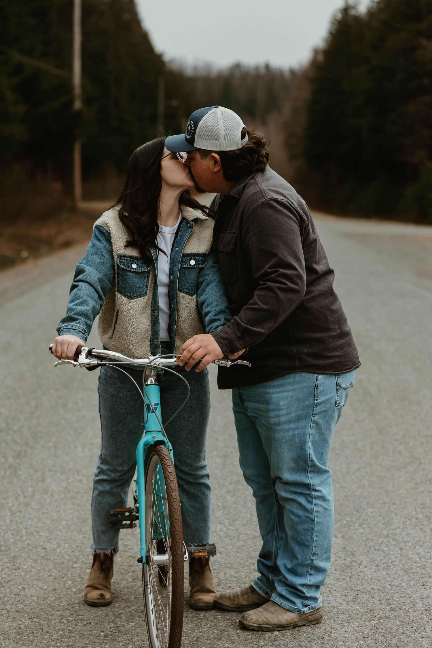 A couple shares a romantic moment on a turquoise bicycle on an empty rural road.