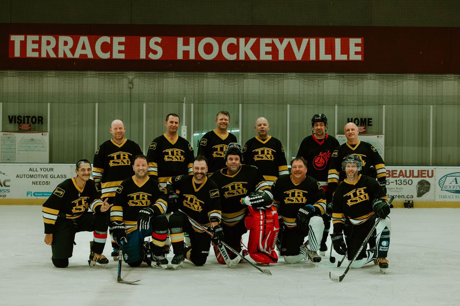Hockey team poses together on ice rink with black jerseys under sign reading TERRACE IS HOCKEYVILLE.