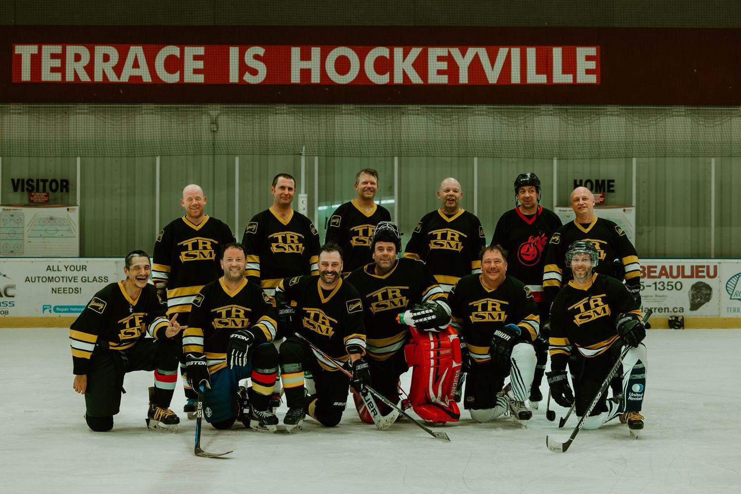 Hockey team in black and yellow uniforms poses together on ice under arena signage.