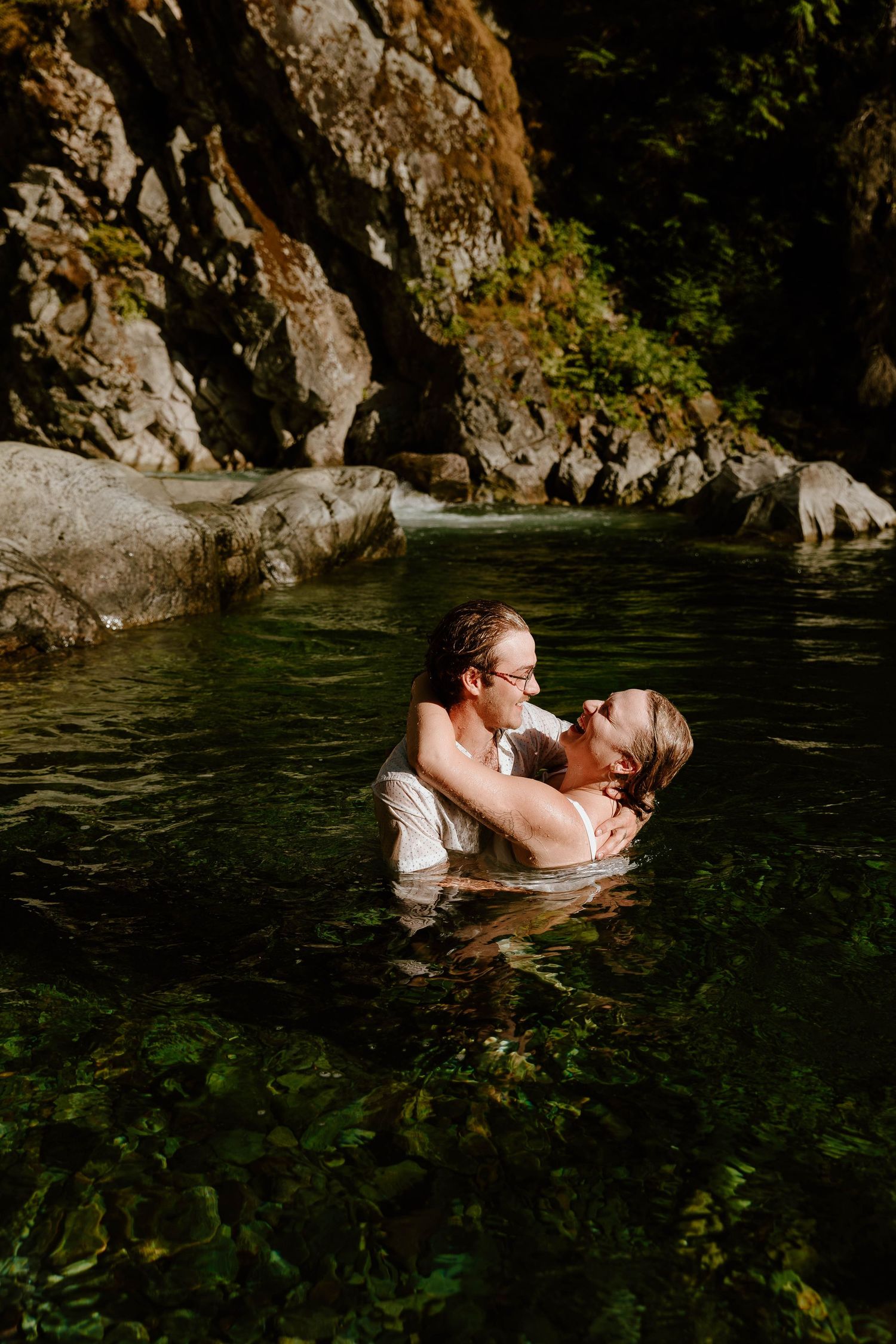A couple shares an intimate moment while swimming in a secluded mountain pool.