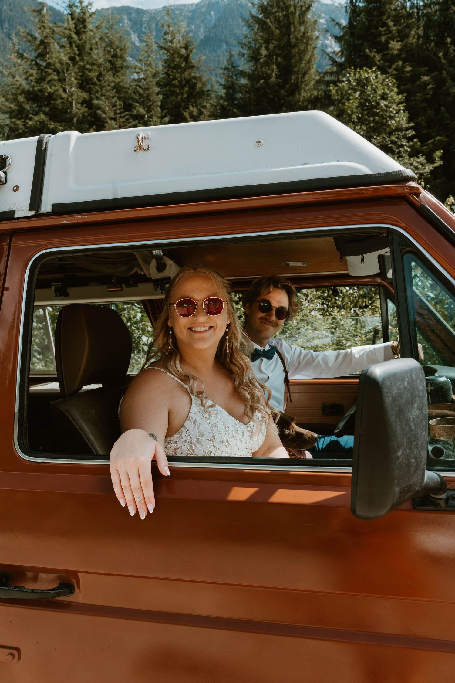A joyful moment captured through the window of an orange vintage van in the mountains.