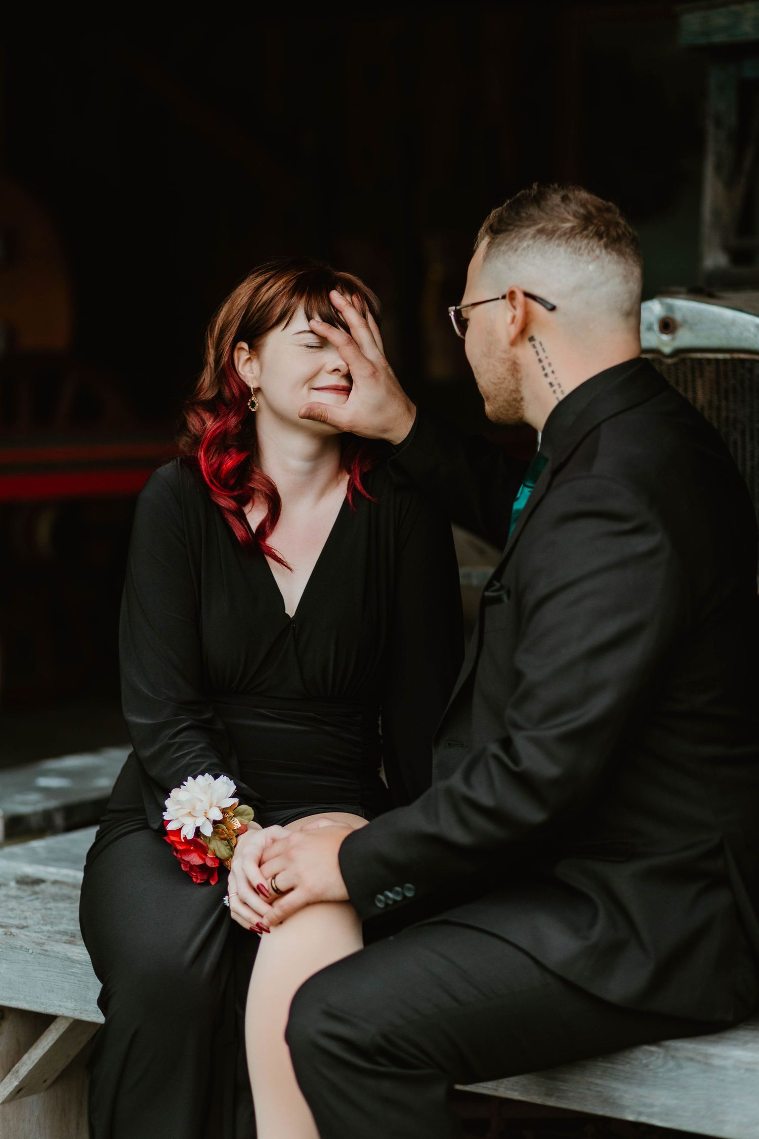 A romantic moment captured between a couple sitting on a wooden bench in formal attire.