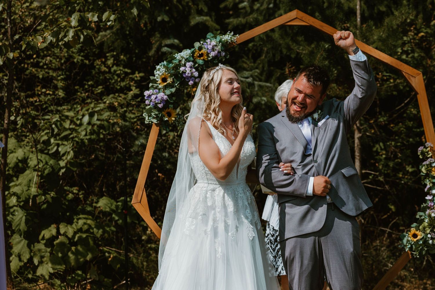 Newlyweds celebrate under wooden hexagonal arch decorated with blue flowers.