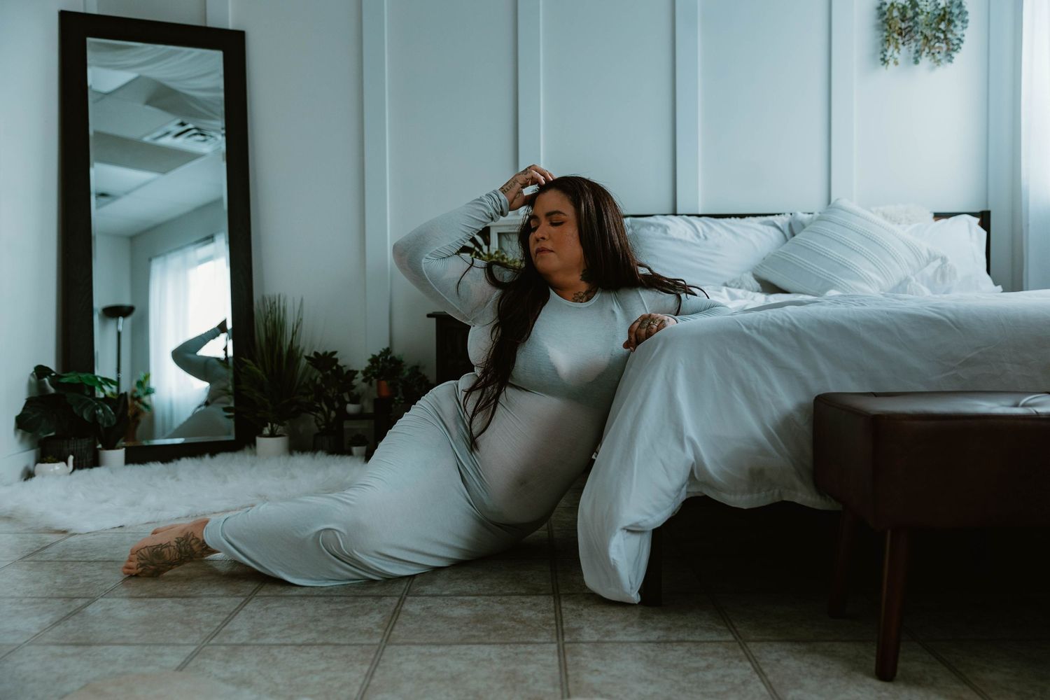 Person in flowing white dress reclining against white bed in minimalist room.