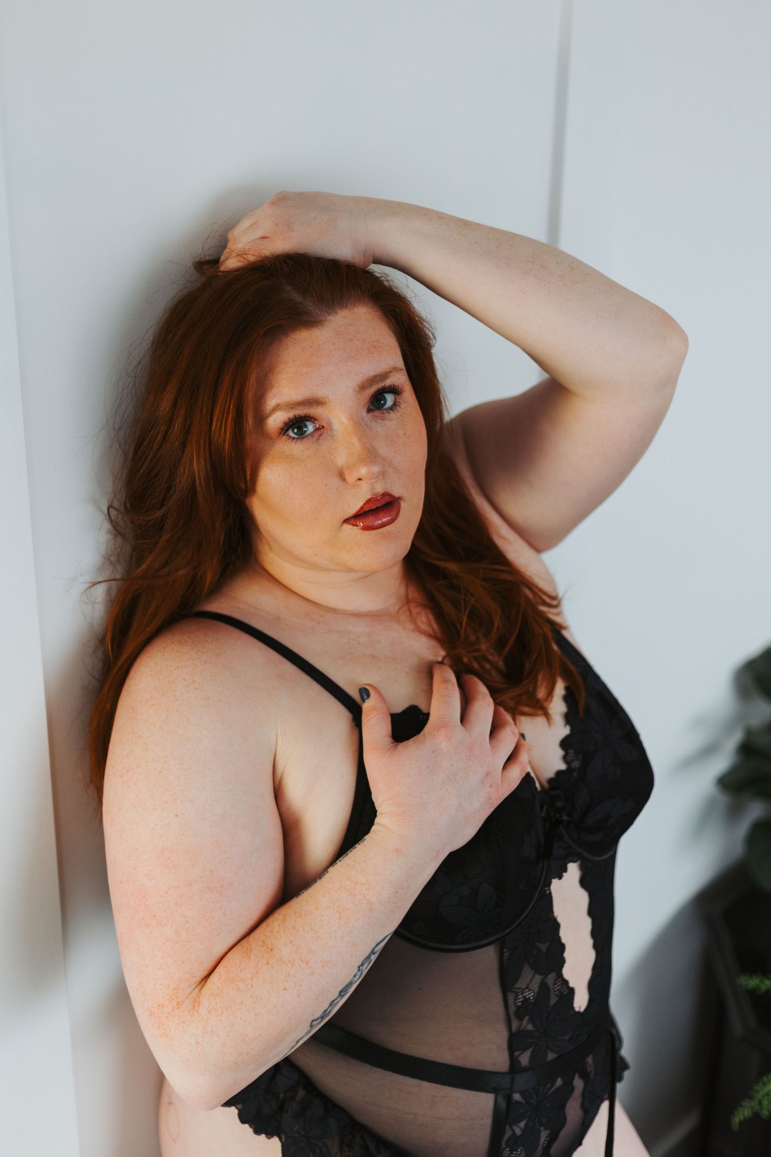 Person in black lace lingerie against white wall in artistic portrait.