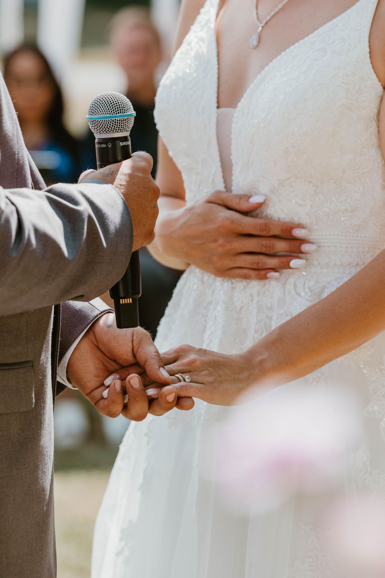 Close-up of hands exchanging wedding rings during ceremony with microphone visible.