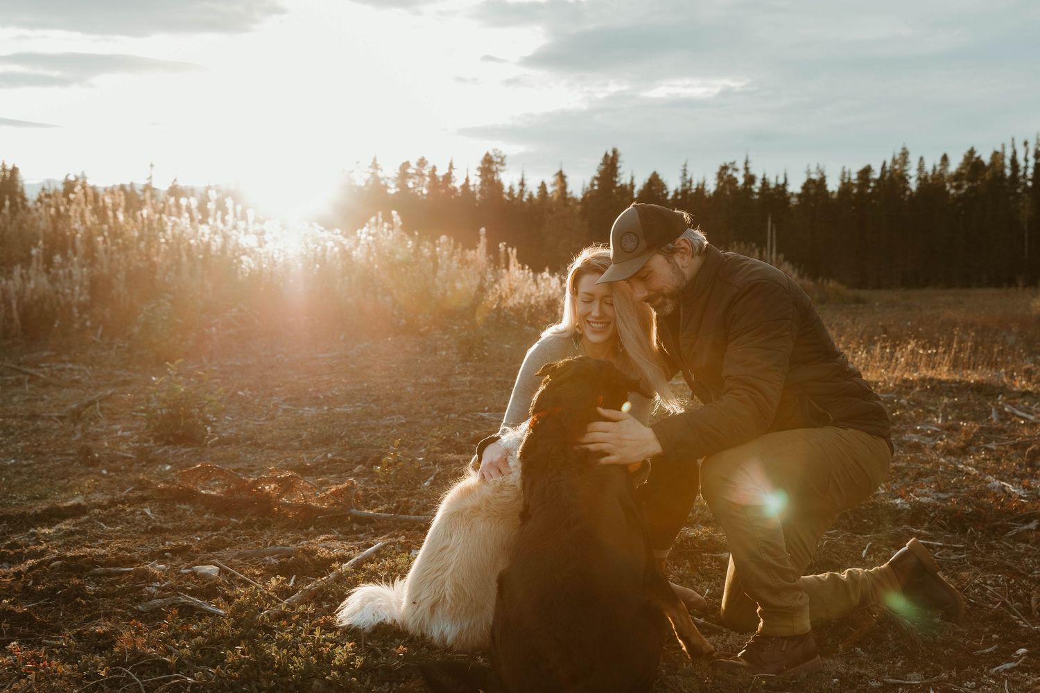 A couple pets their white dog in a golden field during sunset.