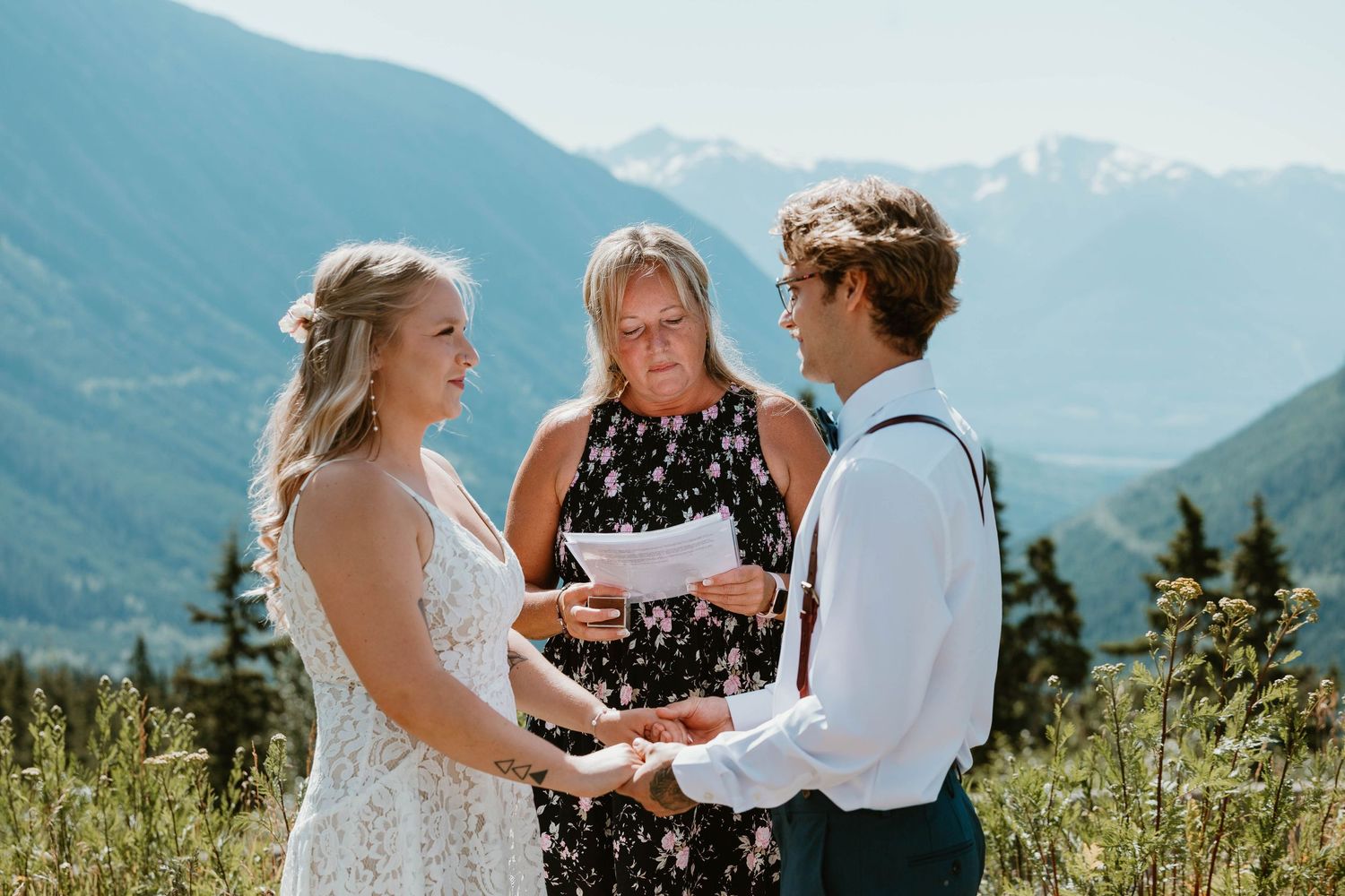 A wedding ceremony takes place on a mountain meadow with dramatic peaks in the background.