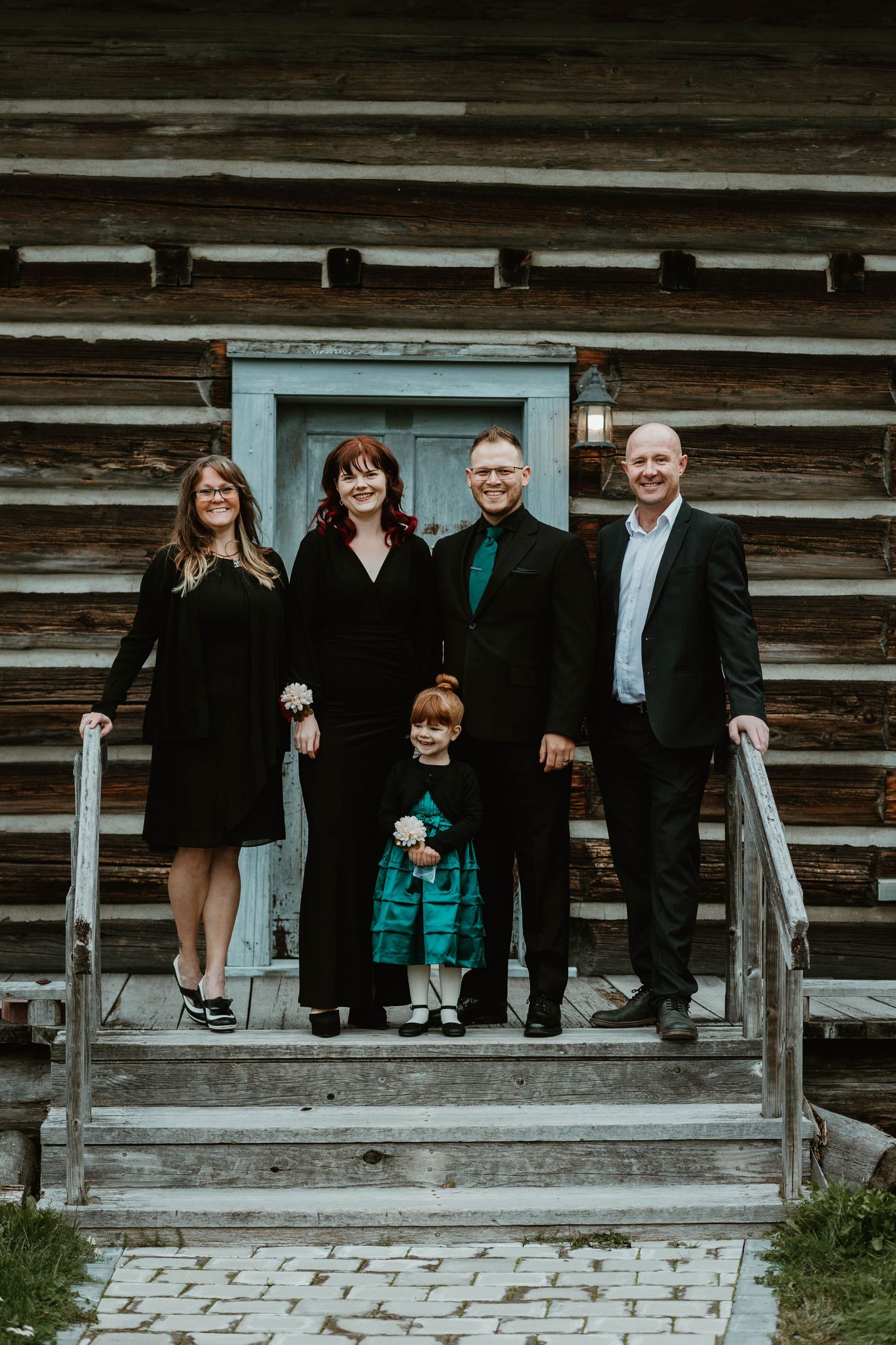 A family group portrait on wooden steps of a rustic cabin with blue door.
