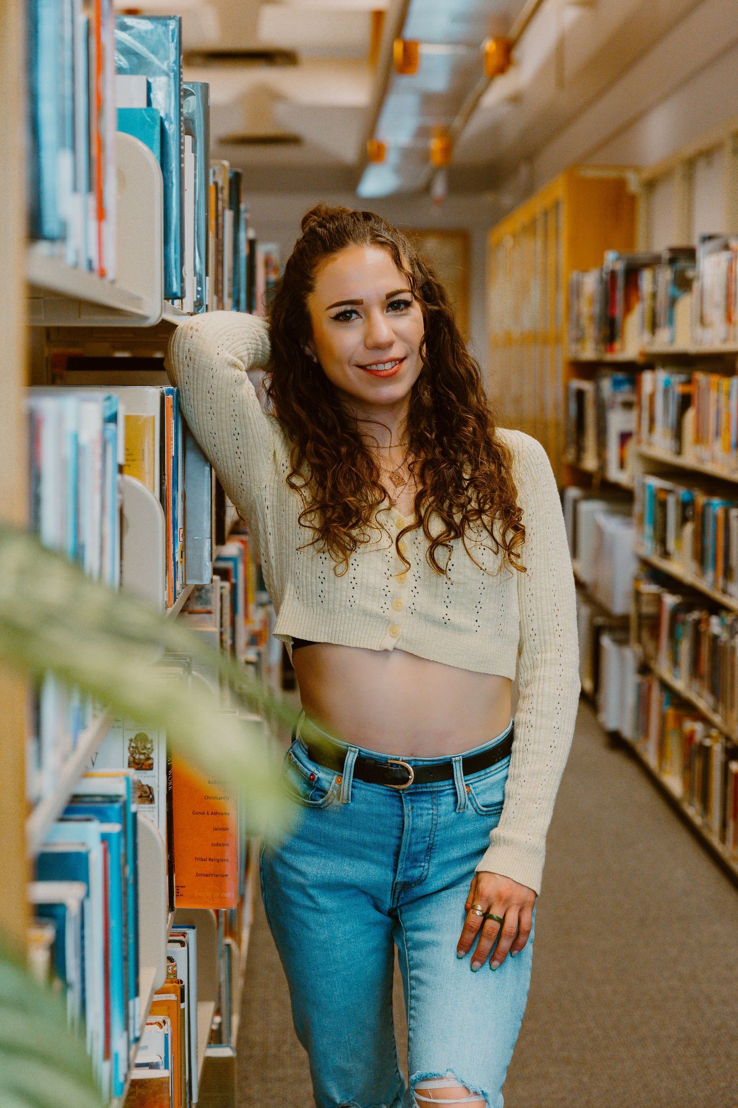 Casual fashion photo taken between library bookshelves showing cropped sweater and jeans outfit.
