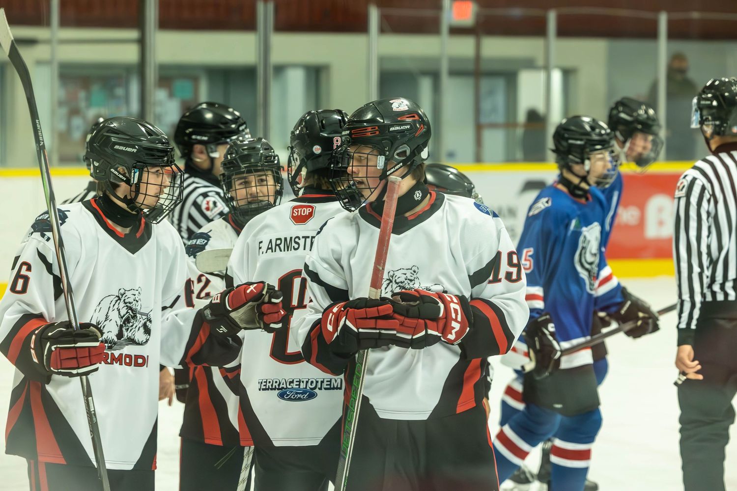 Team huddle of hockey players in white jerseys with referee in background during game break.
