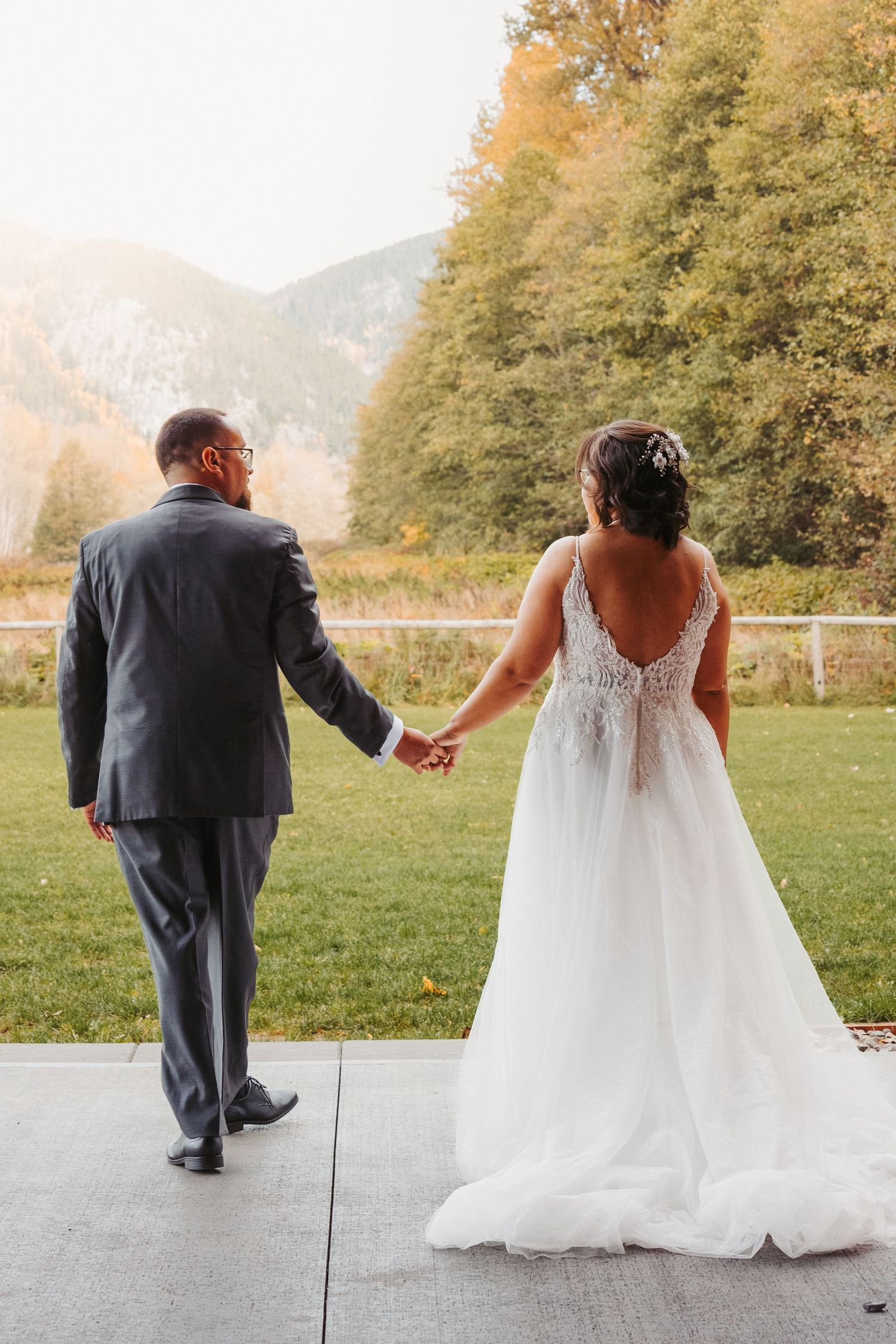Couple in wedding attire holding hands while walking along a mountain path during autumn.