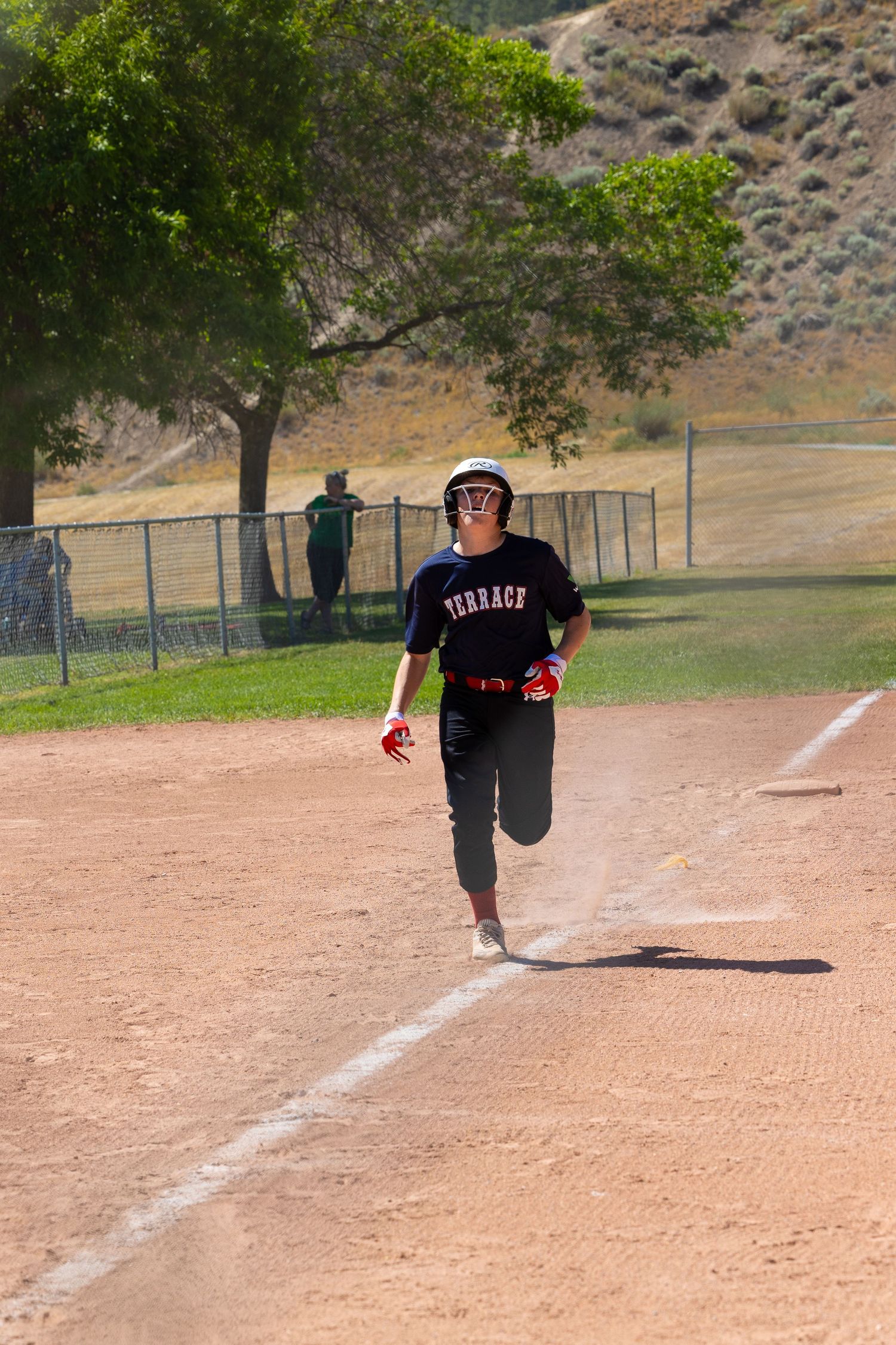 Baseball player in black uniform runs down the baseline on a dirt field with mountains in the background.