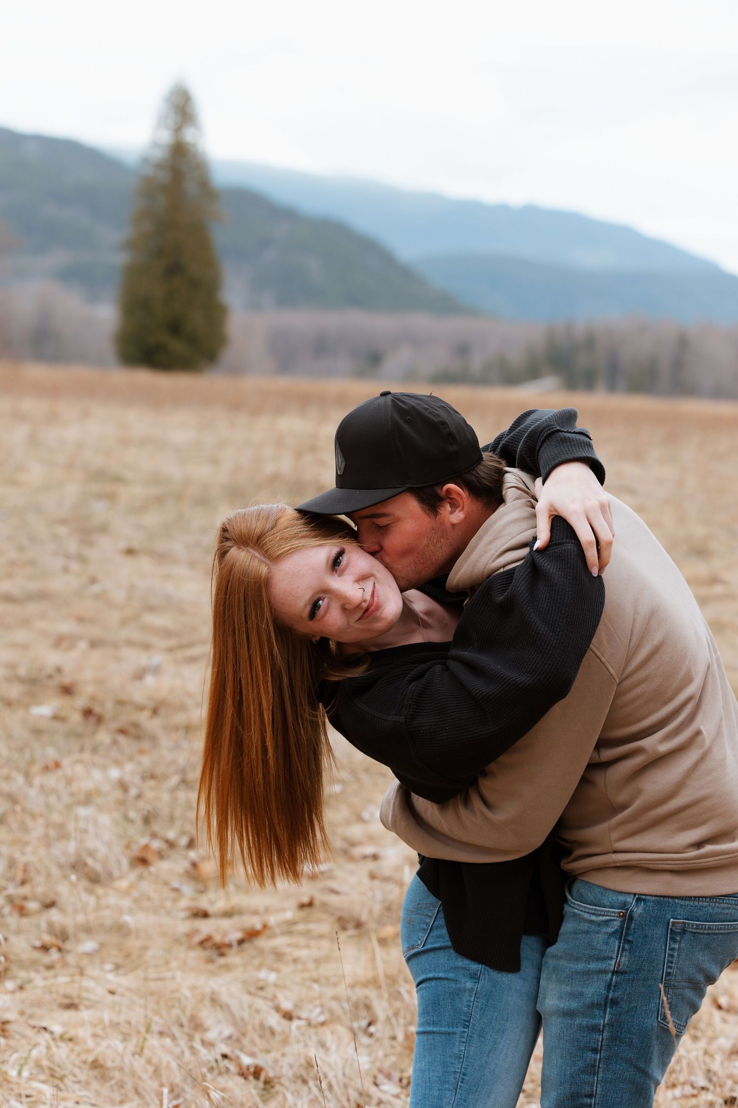 Playful couple embraces and laughs together in mountain field setting.
