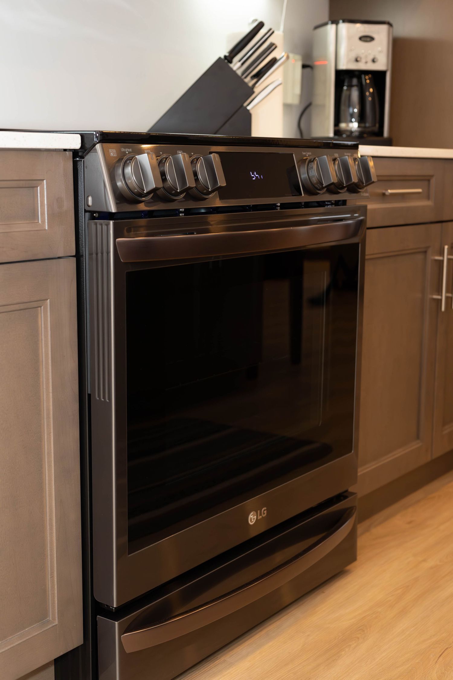 Black LG electric range with glass top and digital controls nestled between taupe cabinets in modern kitchen.