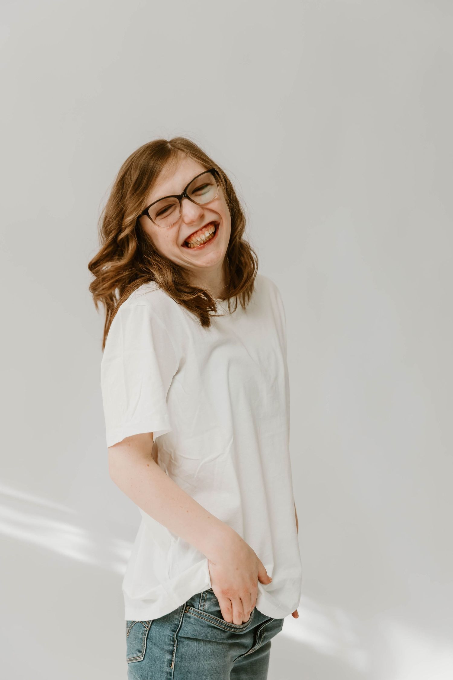 A person wearing glasses and a white t-shirt smiles joyfully against a light gray background.