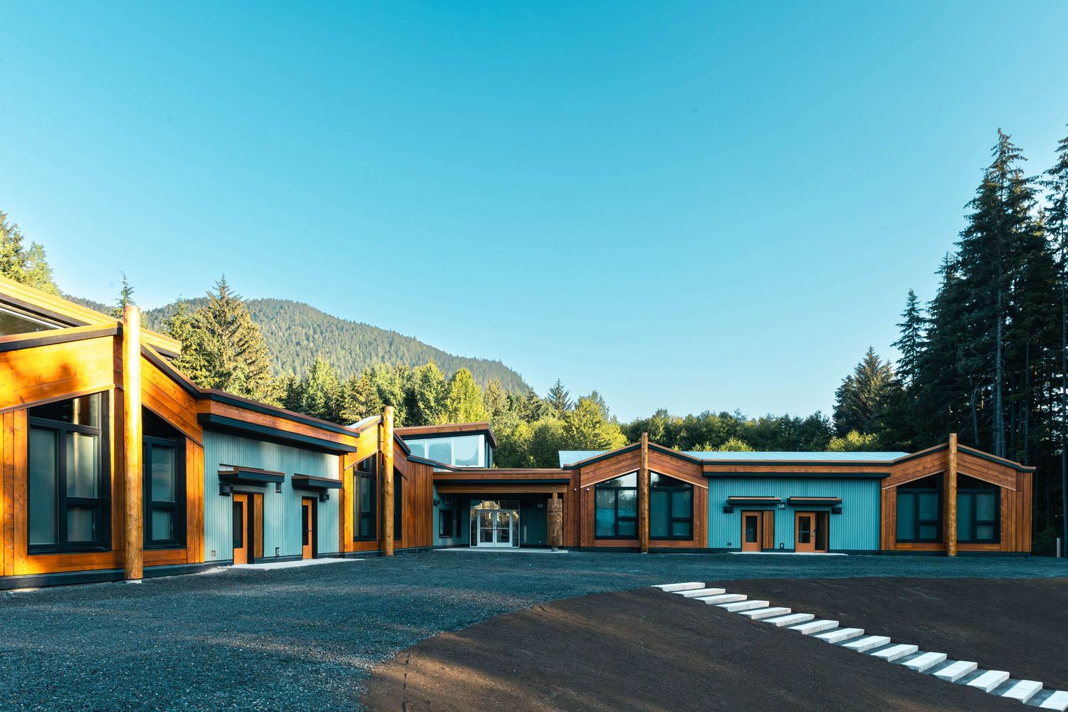 Modern orange and gray modular buildings with slanted roofs set against mountain backdrop under clear blue sky.