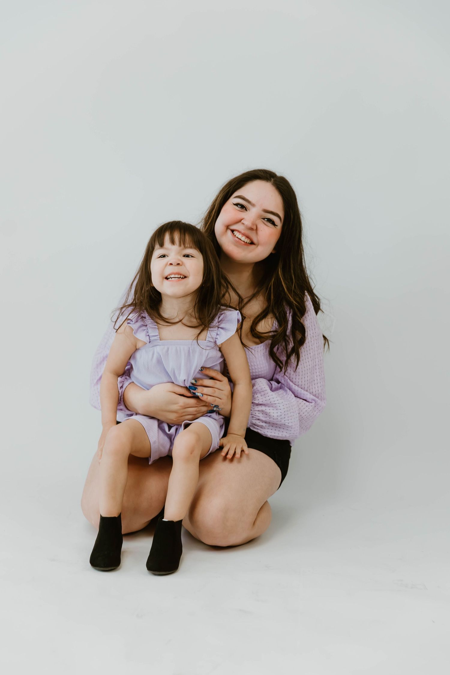 Two people in matching purple outfits sit and smile together against a white background.