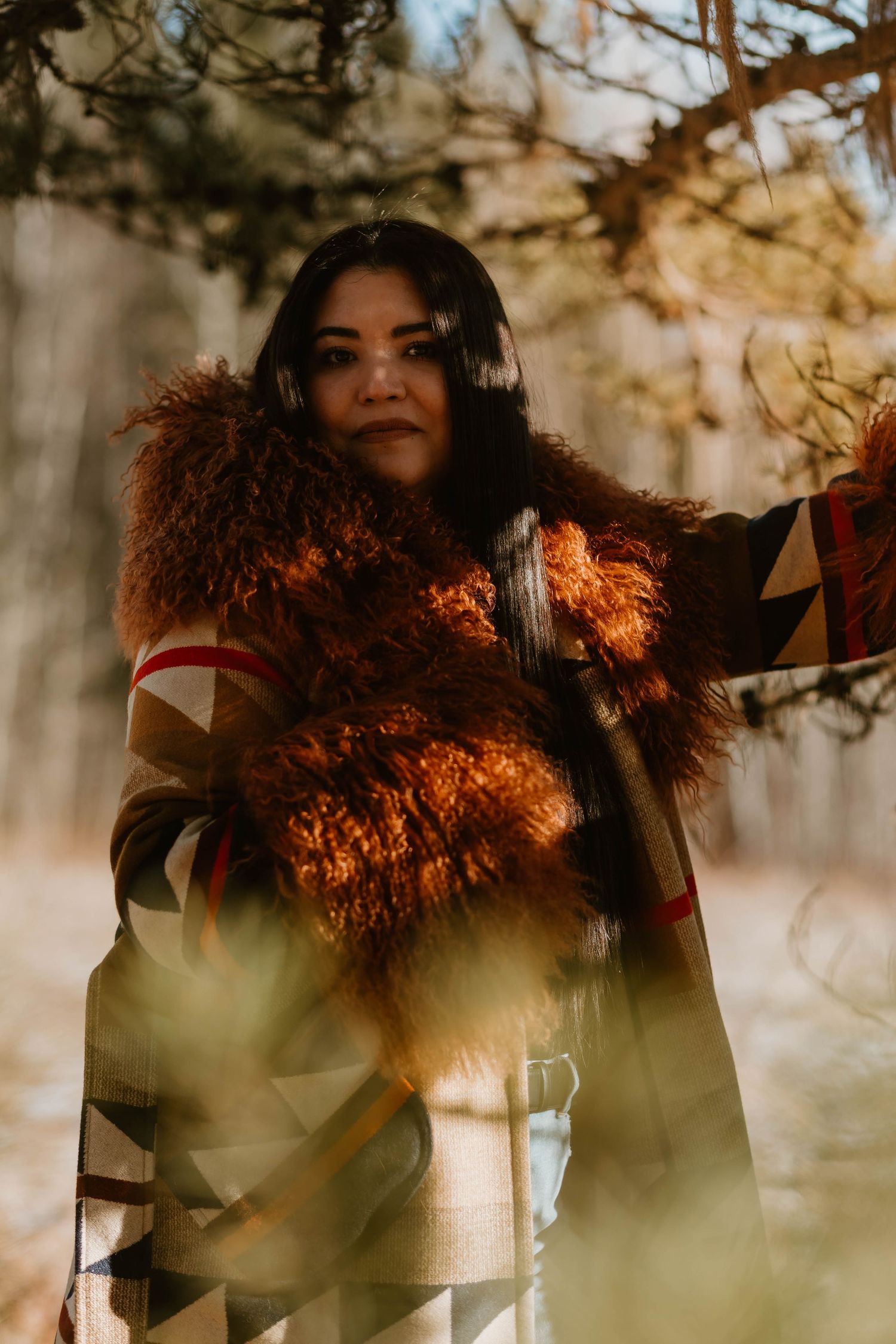 Person wearing patterned coat with fur trim photographed in warm golden forest light.