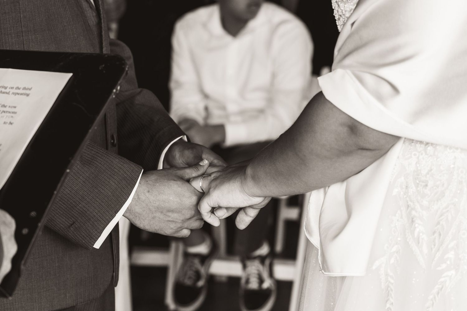 Black and white close-up of hands exchanging rings during wedding ceremony.