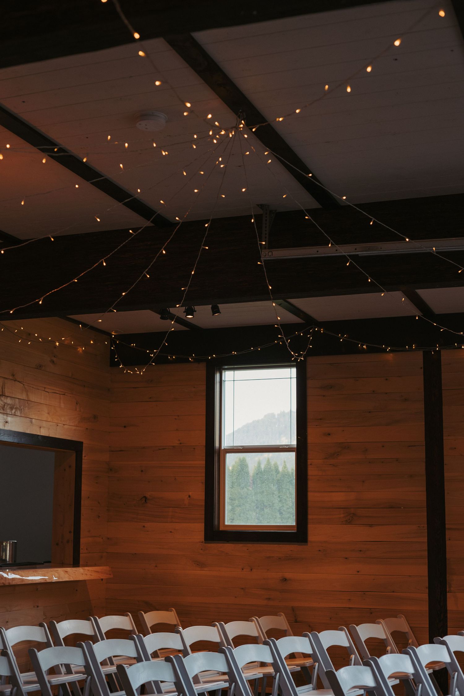 Rustic wooden interior room with string lights decorating the ceiling and folding chairs set up in rows.