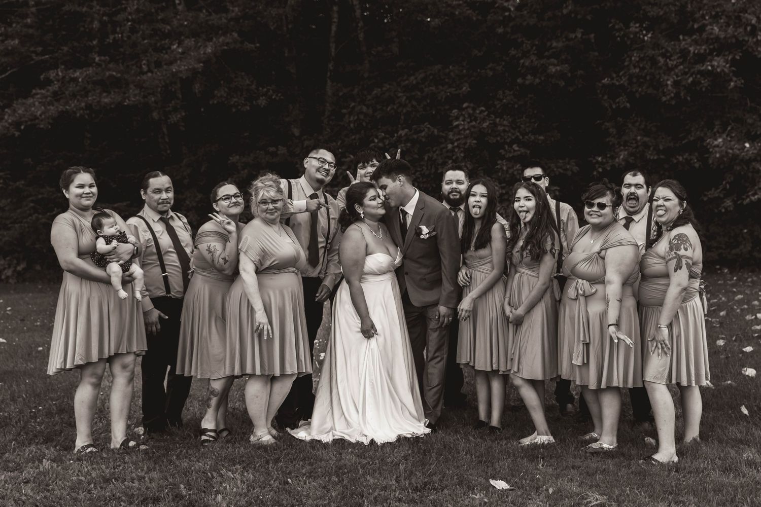 Wedding party poses together in matching dusty rose bridesmaids dresses for outdoor group photo.
