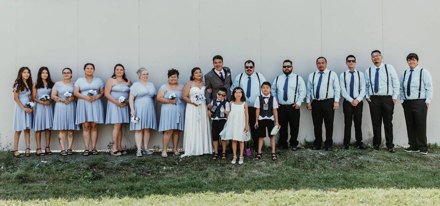Wedding party lined up against grassy hill wearing coordinated light blue and grey attire.