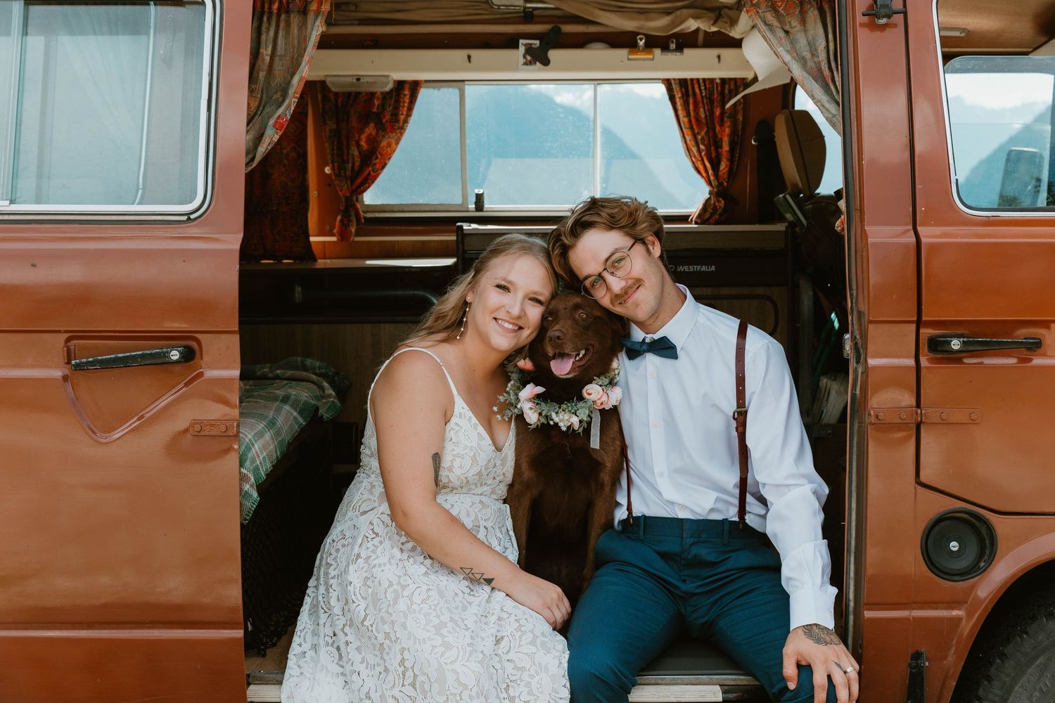 A couple and their dog relaxing inside a vintage orange van on their wedding day.