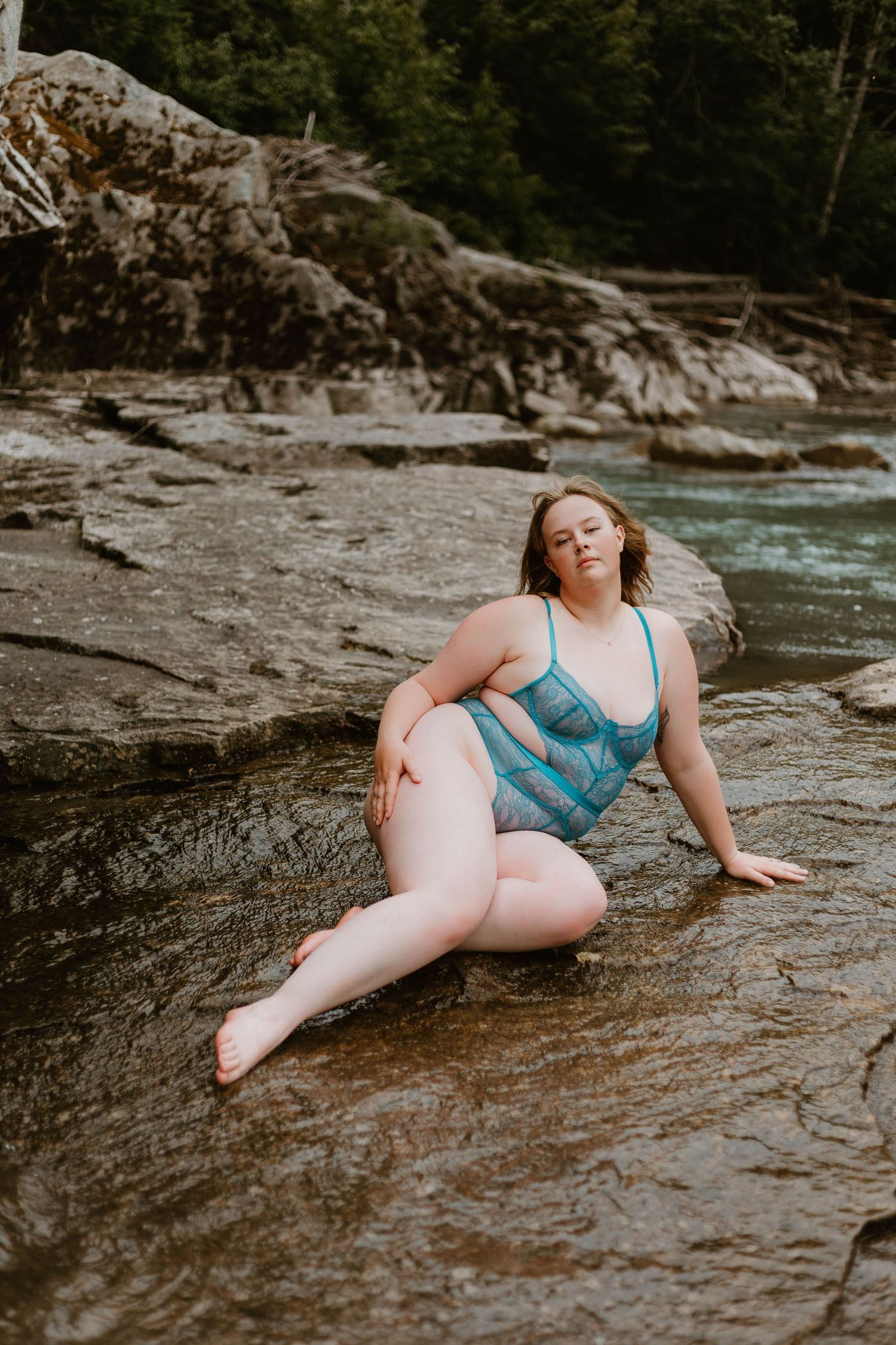 Person in blue lingerie poses on rocky riverbank.