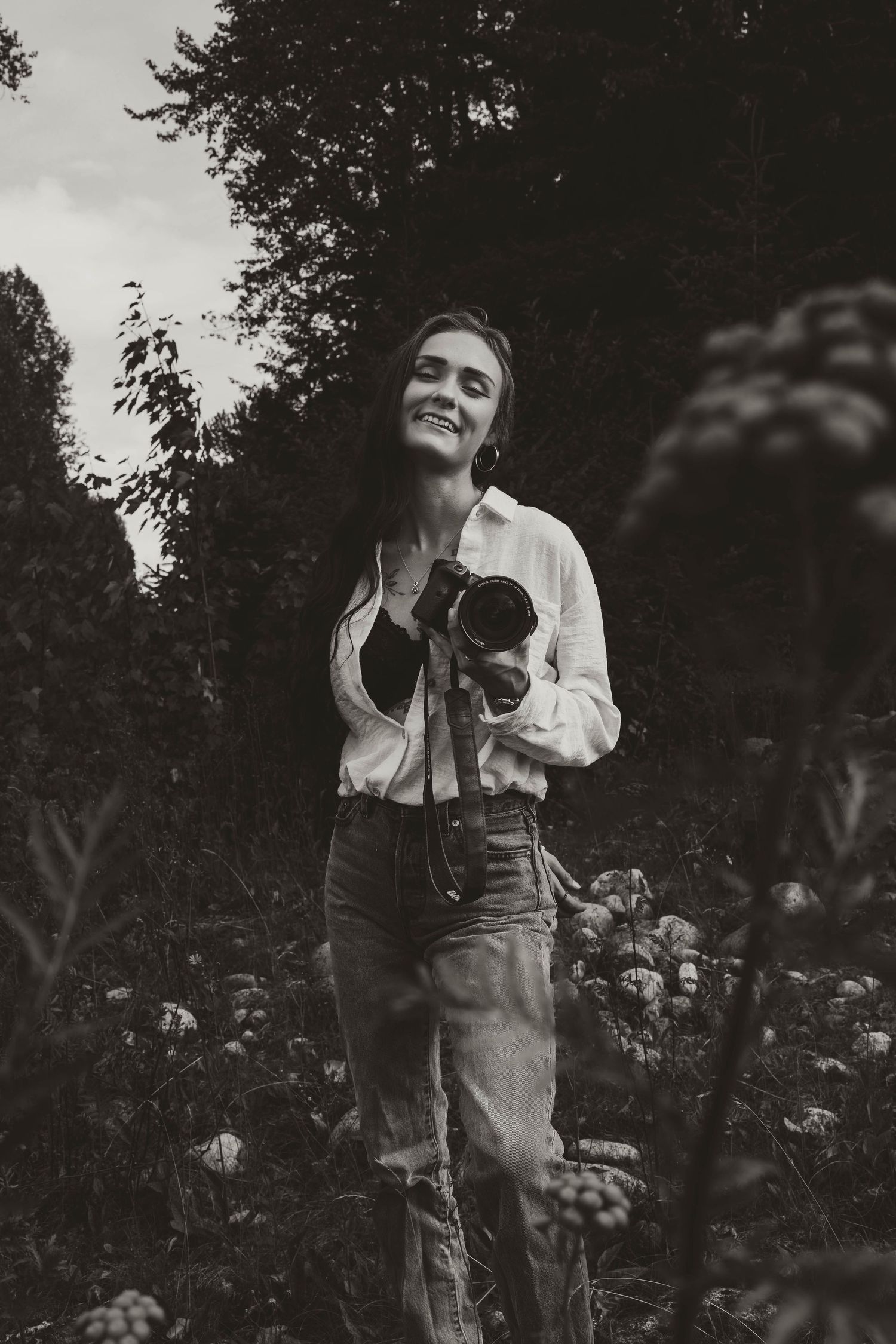 A black and white portrait of a photographer holding their camera in a garden setting.