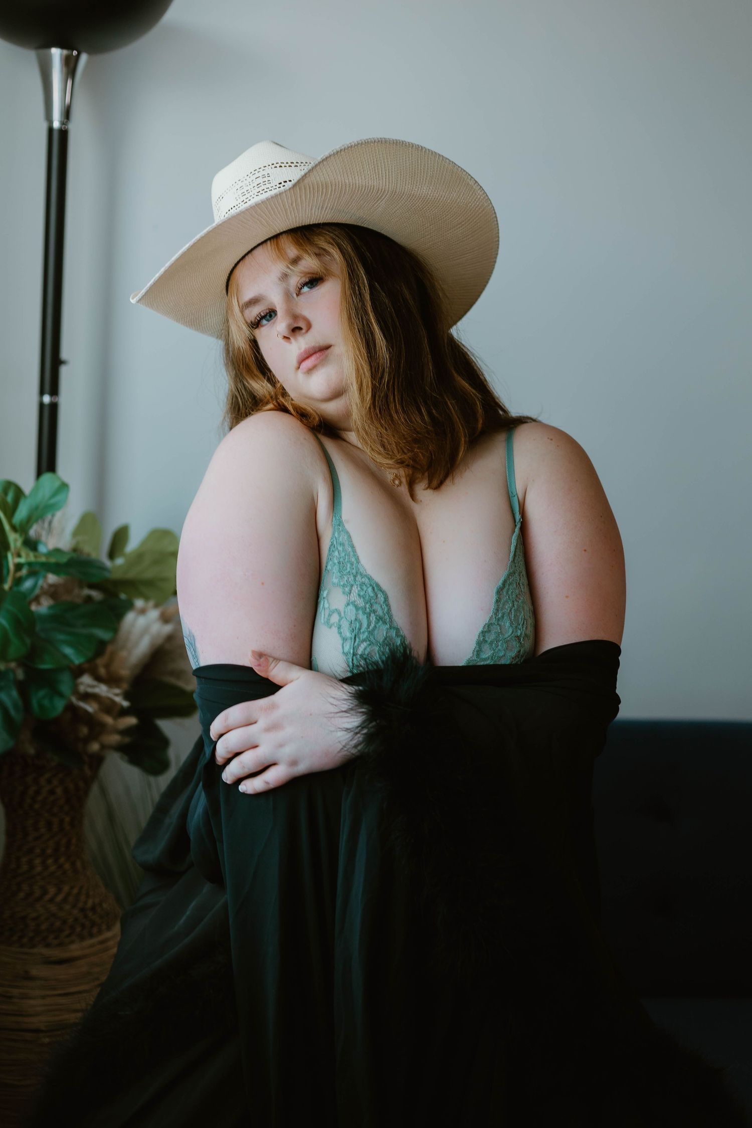 Artistic indoor boudoir shot featuring teal lingerie and a beige wide-brimmed hat against a minimalist background.