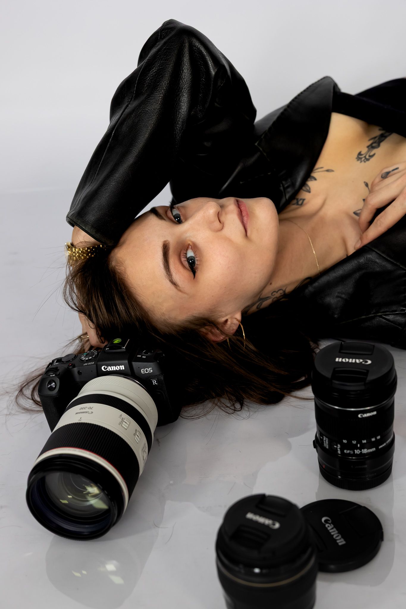 Artistic black and white portrait series showing a person lying down with various Canon camera lenses arranged nearby.
