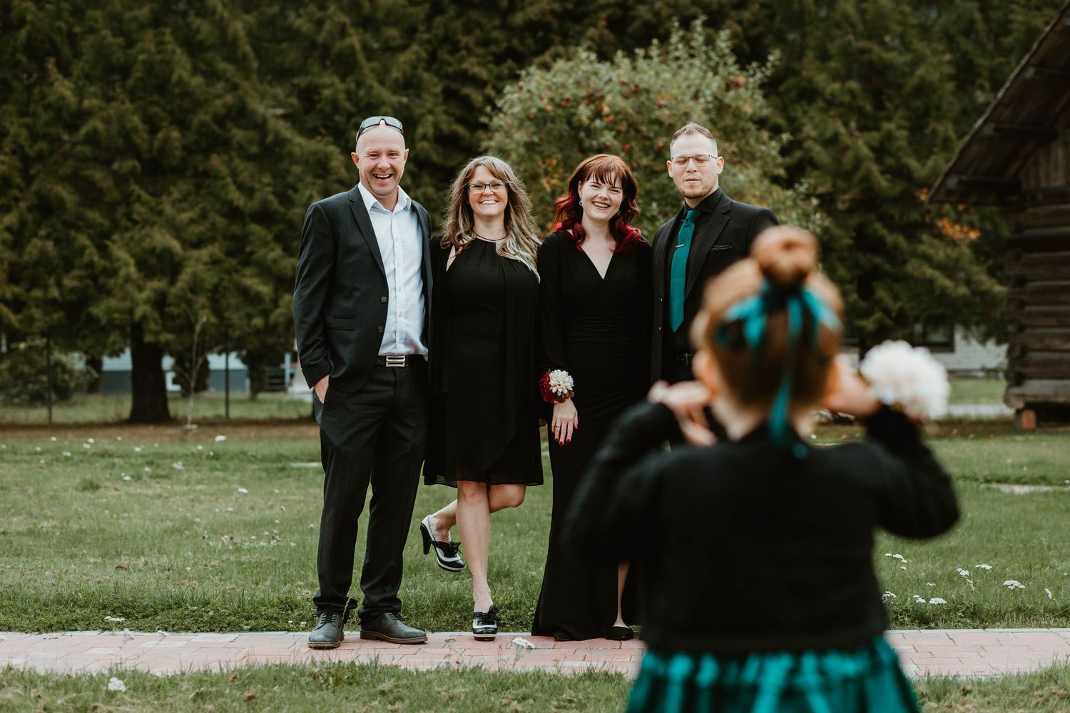 A group watches as a child in a teal dress poses for photos on a grassy lawn.