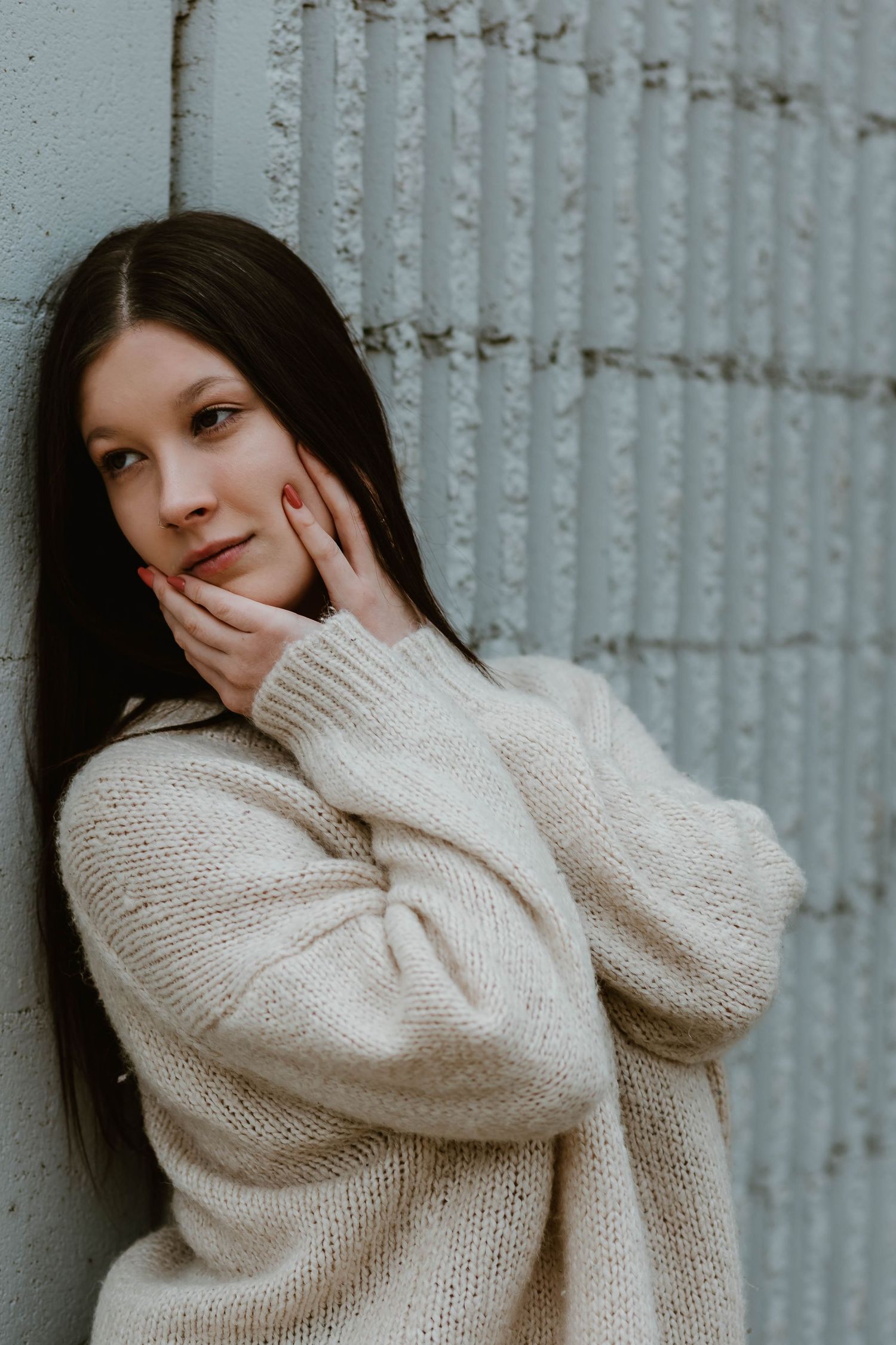 Person in cozy cream sweater poses against textured wall in natural lighting.