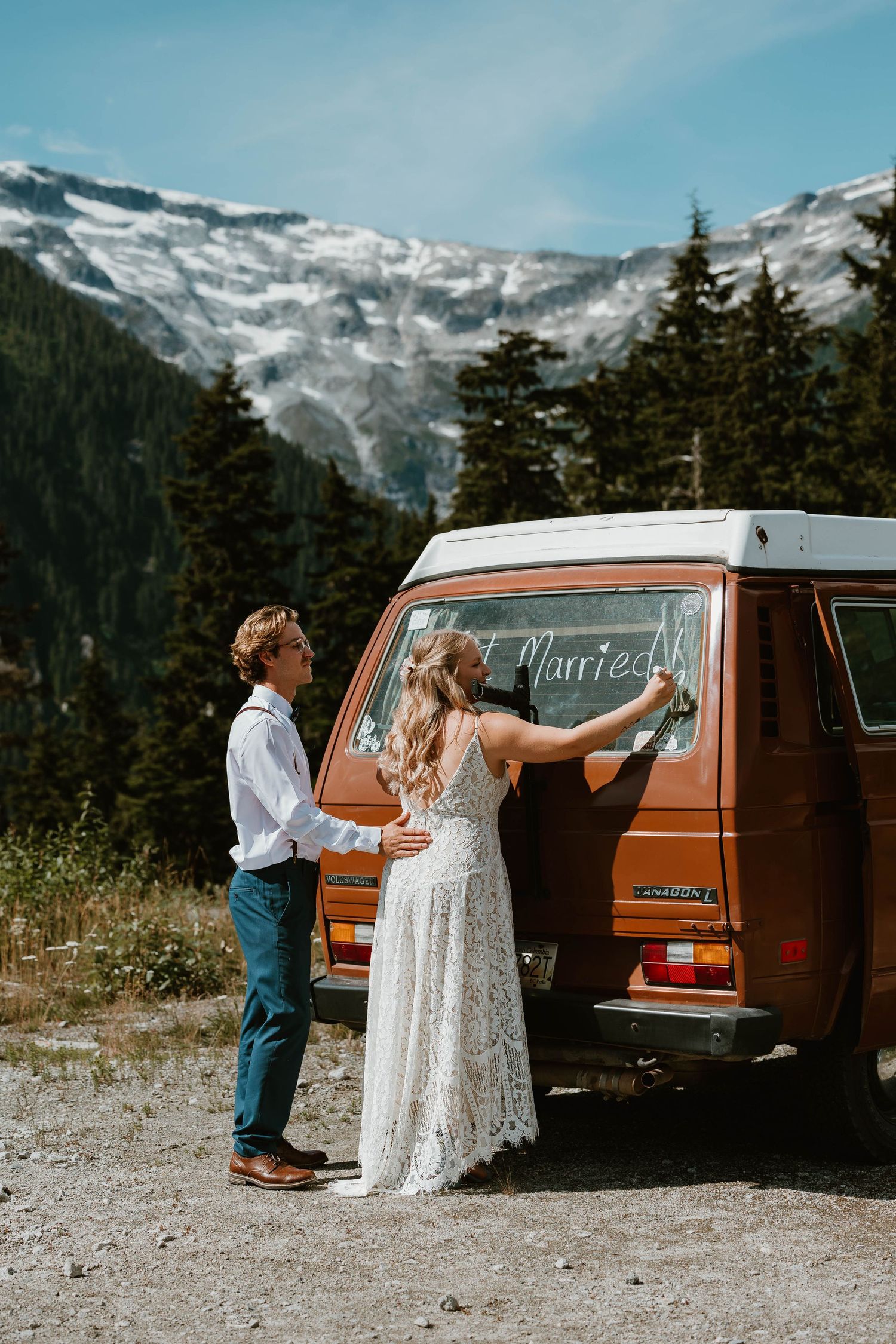 Couple writing on vintage orange van with snowy mountain peaks in background.